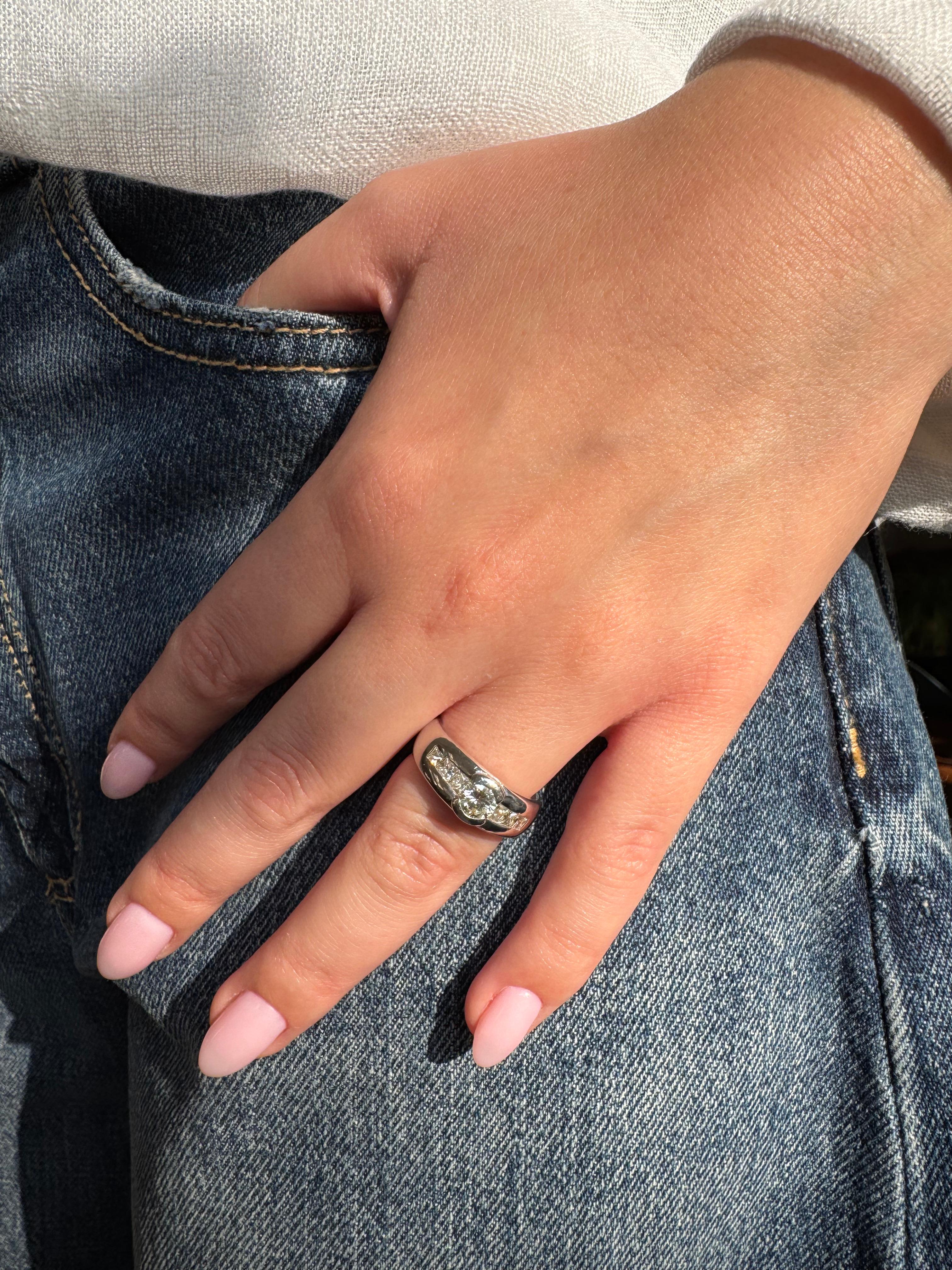 This sleek and modern white gold band combines bold presence with refined sparkle. Cast in 18K (750‰) white gold, the gently tapered shank supports a bezel-like setting that cradles a brilliant round diamond of approximately 0.55 carat. Flanking the