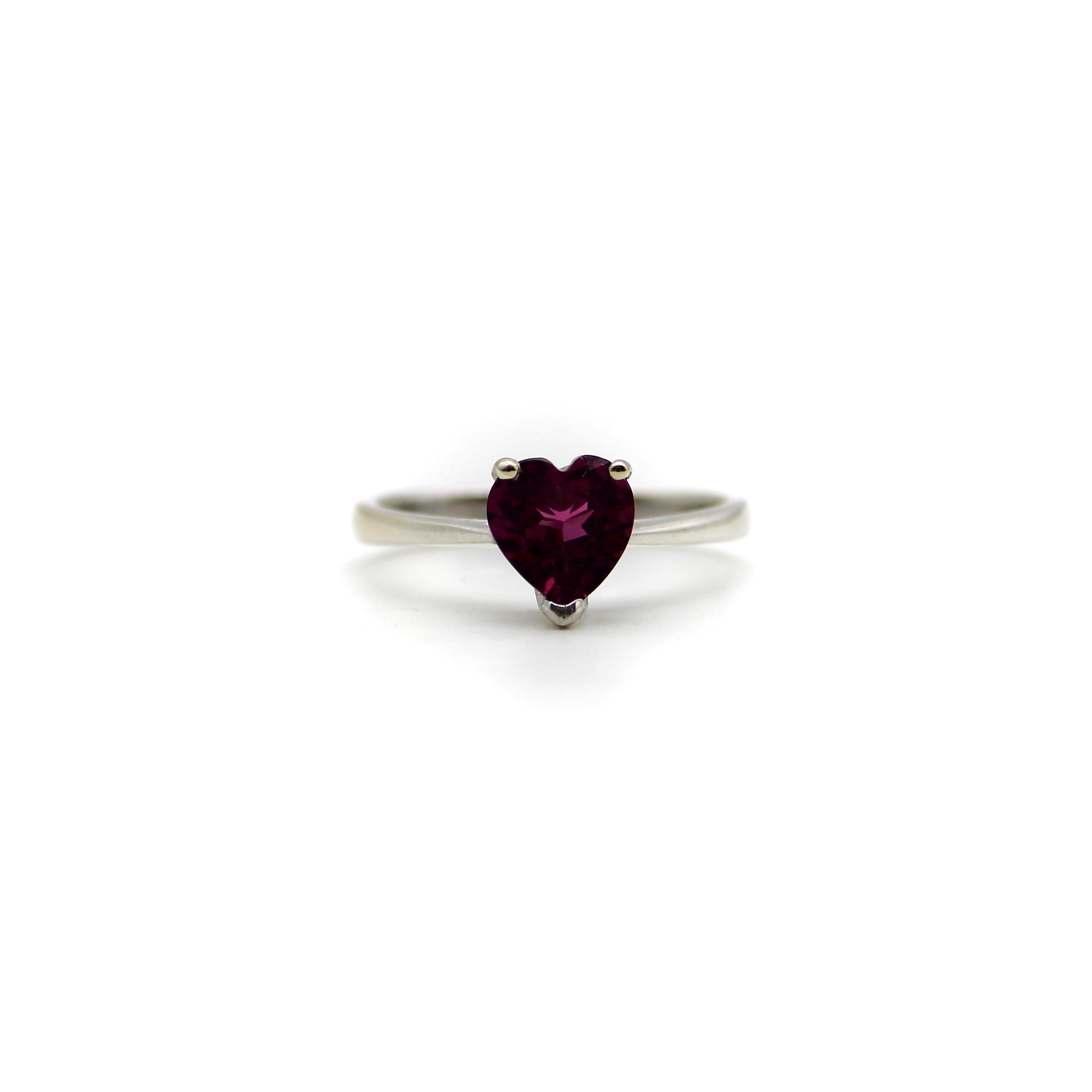 This 18k white gold ring features a beautifully colored heart-shaped garnet. The garnet is a saturated deep magenta, with facets that sparkle in many different hues of pink and red. It is prong set with three prongs; the back of the carriage or