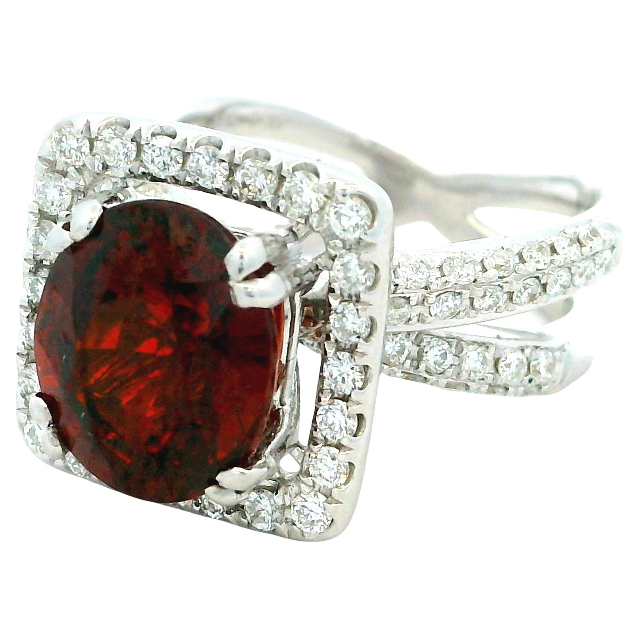 Questo anello da cocktail contemporaneo è realizzato in oro bianco 18 carati e presenta un vivido granato dal taglio ovale del peso di circa 4,00 carati. La gemma rosso intenso è incorniciata da una scintillante aureola di diamanti rotondi a taglio