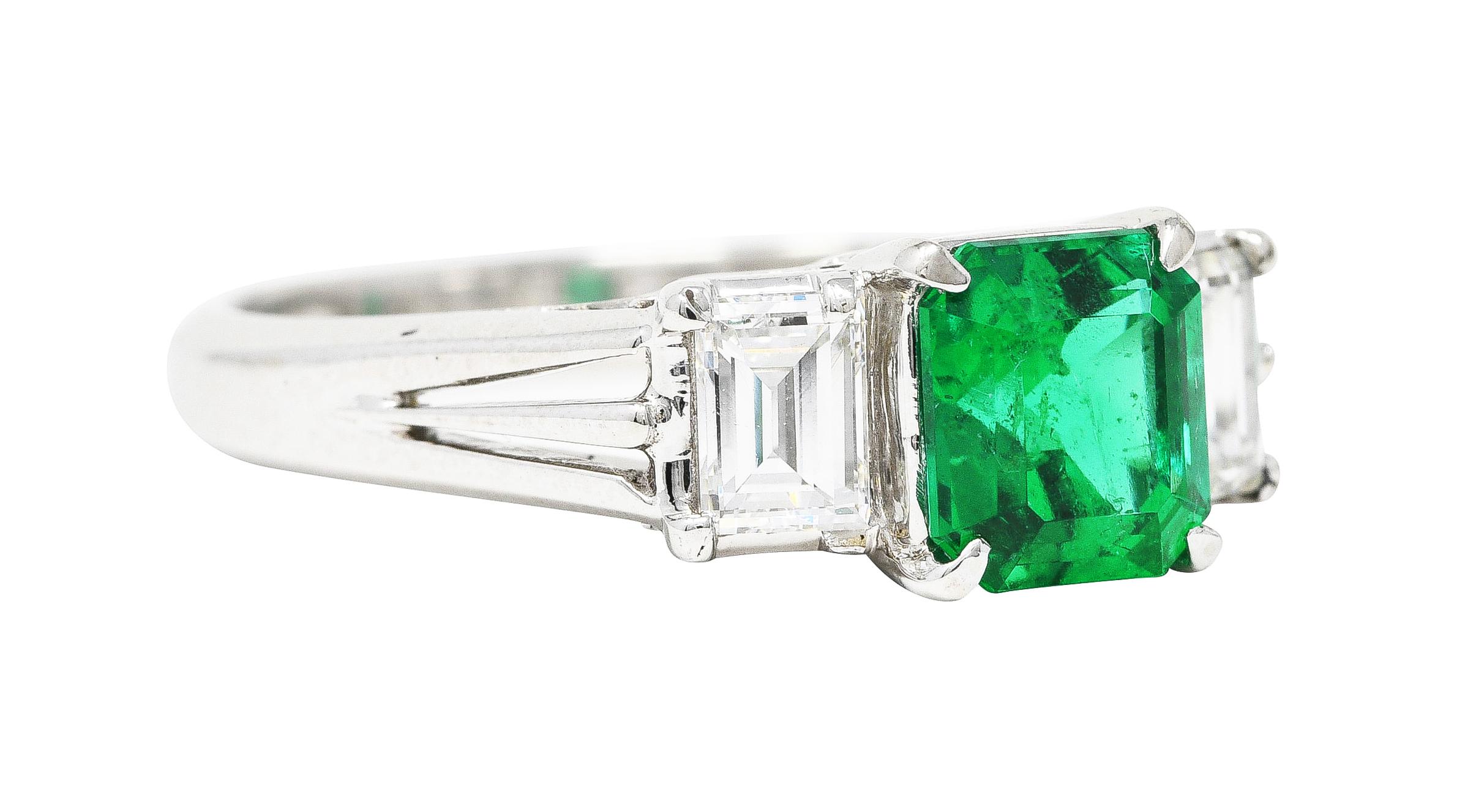 Ring is prong set to front by three gemstones in a stepped form. Centering an emerald cut Colombian emerald weighing 1.24 carats. Transparent and richly green in color - natural inclusions with moderate clarity enhancement (F2). Flanked by baguette
