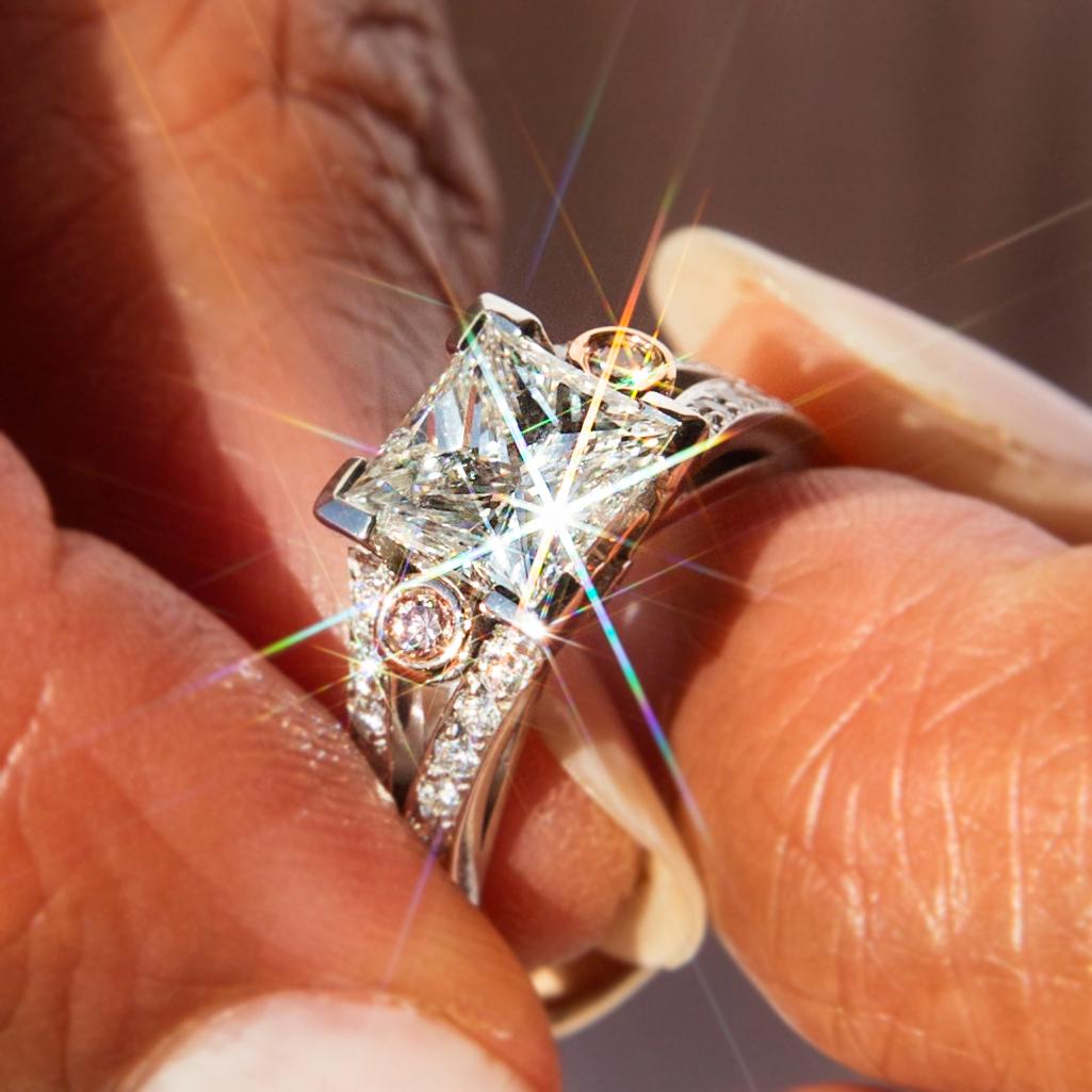 Forged with love and care in 18 carat gold, this stunning contemporary ring boasts an incredible 2.04 carat princess cut diamond in a partial rubover setting flanked by an irresistible duo of rose gold rubover set pink diamonds and two rows of