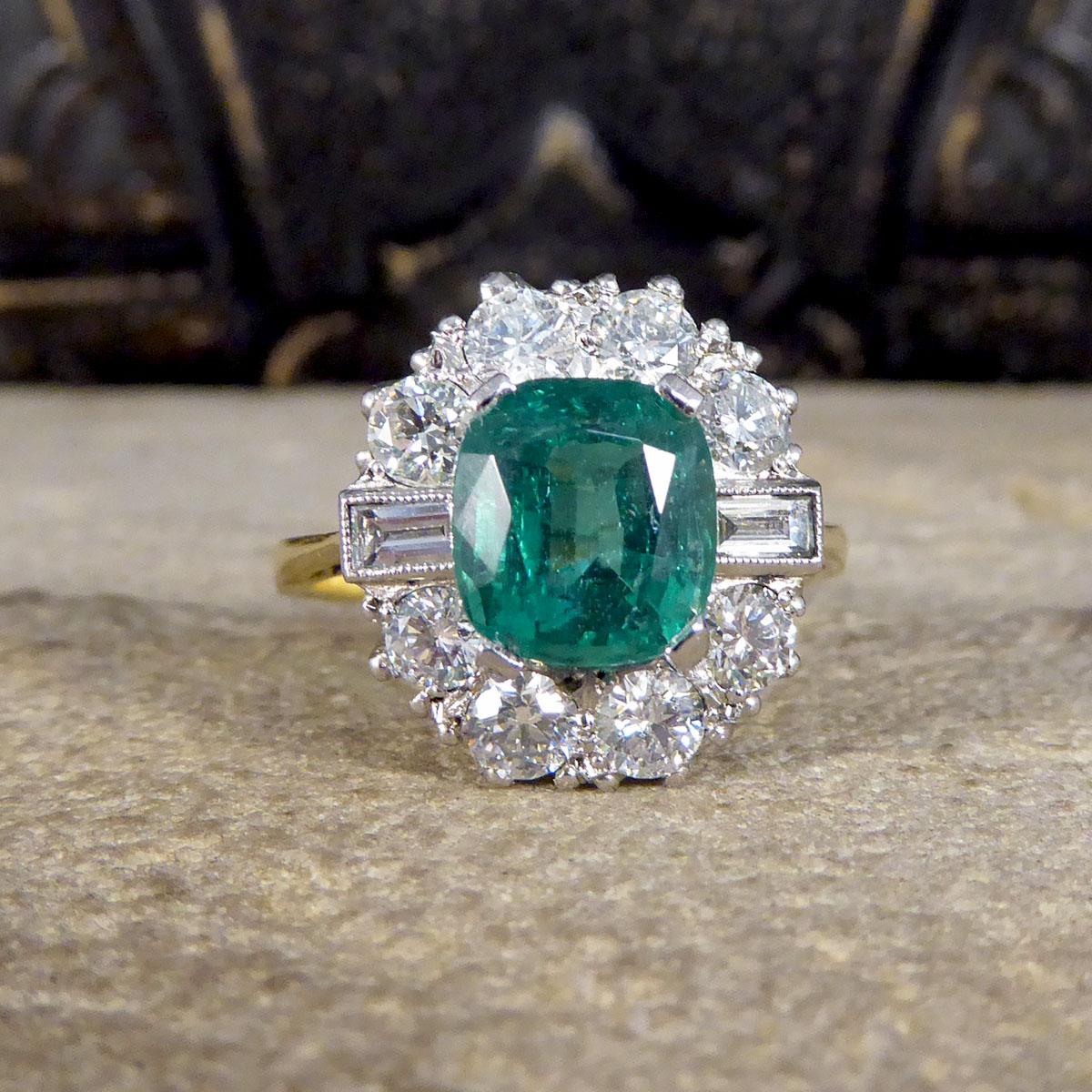 This gorgeous contemporary ring features a mesmerising Emerald gemstone with a great vibrant colour and small surface inclusion on the top. It has a halo of four modern brilliant cut Diamonds above and below, with two baguette cut Diamonds