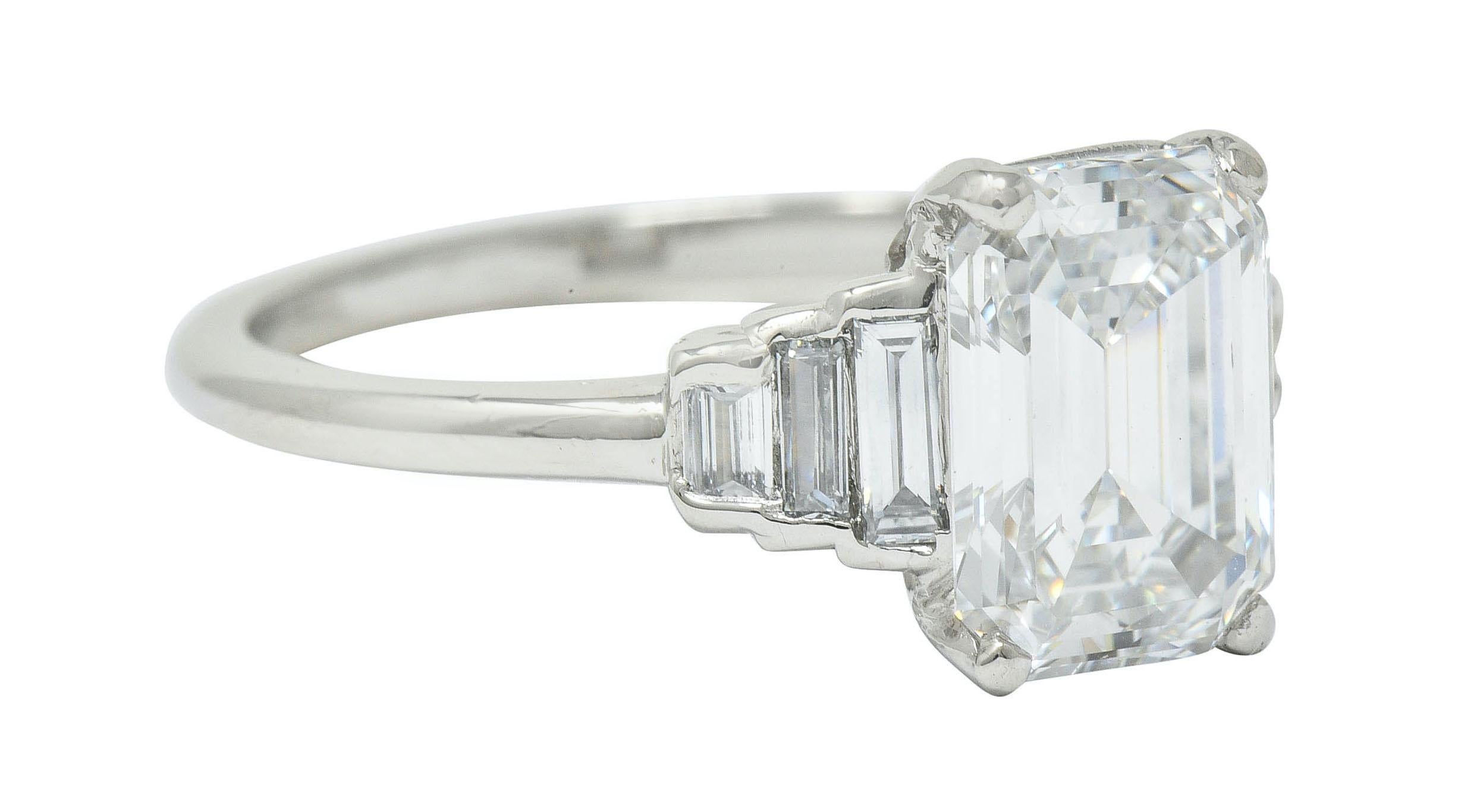 Centering a basket set emerald cut diamond weighing 2.00 carats; remarkable F color with VVS1 clarity

Flanked by stepped shoulders half bezel set with baguette cut diamonds 
weighing approximately 0.20 carat; eye-clean and white

Tested as