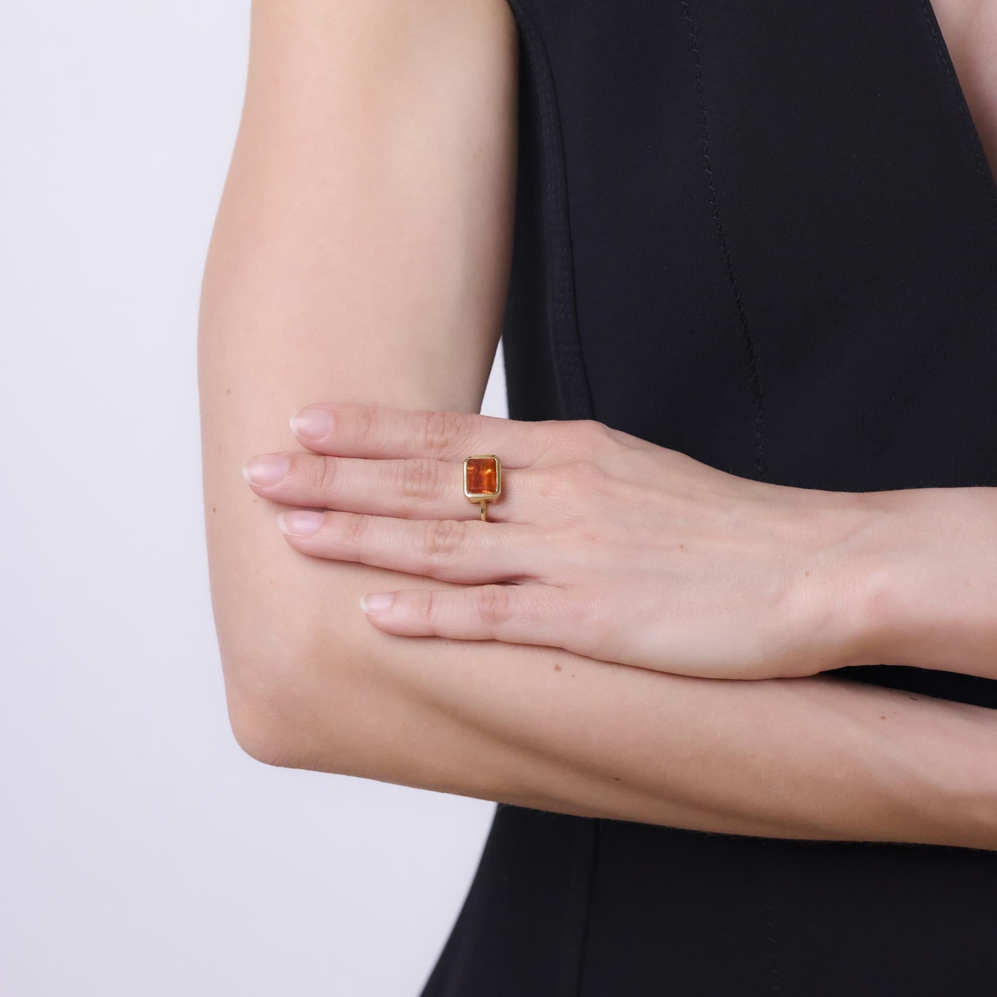This contemporary ring by Hubert, crafted in the 2010s, features an emerald cut fire opal weighing approximately 2.30 carats. The vivid stone is set in warm 18k yellow gold, offering a clean, modern silhouette that highlights the opal's fiery glow.