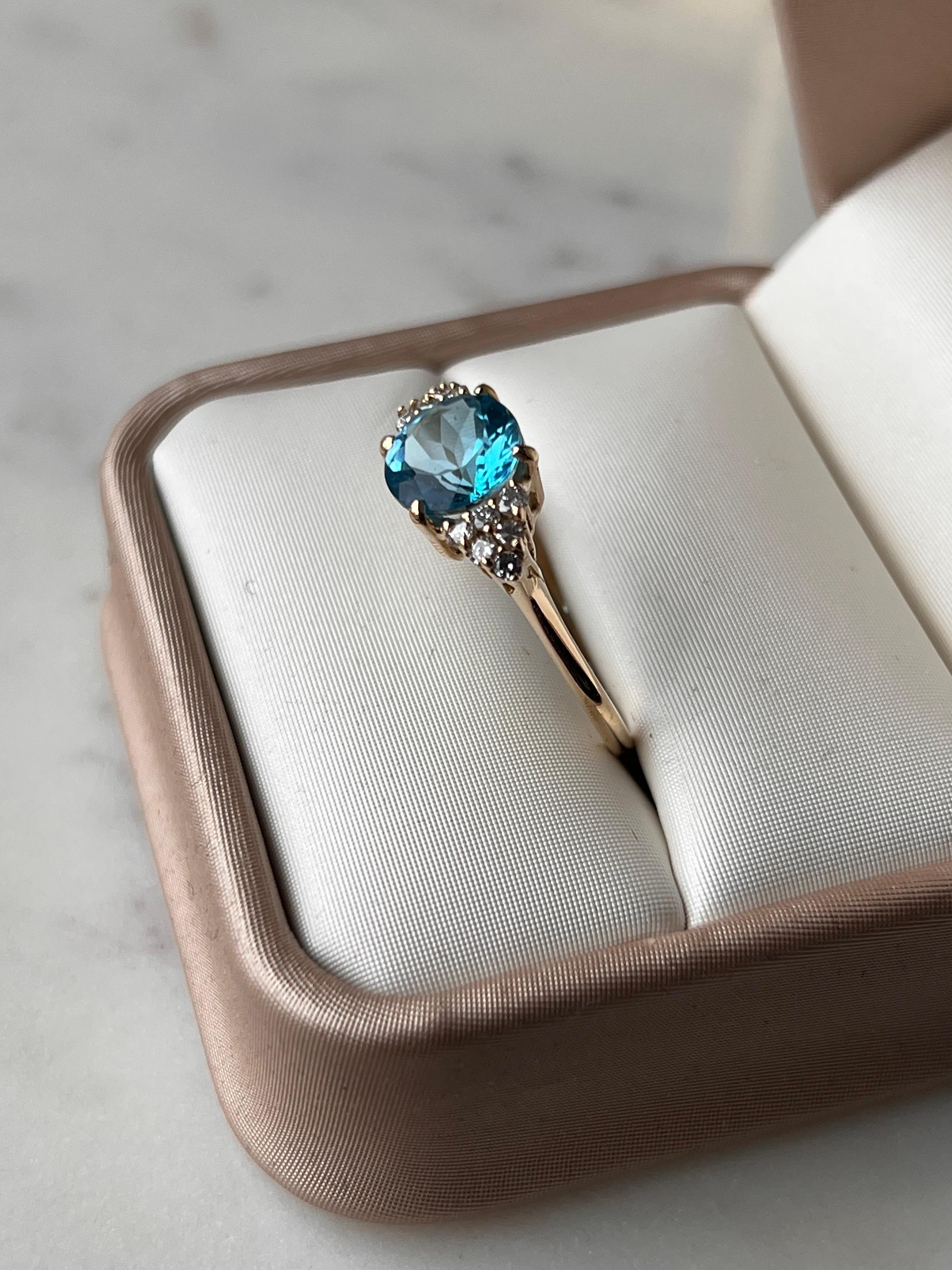 Une bague contemporaine en or jaune 14 carats présente en son centre une topaze bleue ronde de 8 mm de diamètre, d'environ 2,39 carats, entourée de douze diamants ronds étincelants de taille brillante. Les diamants, d'une taille totale d'environ