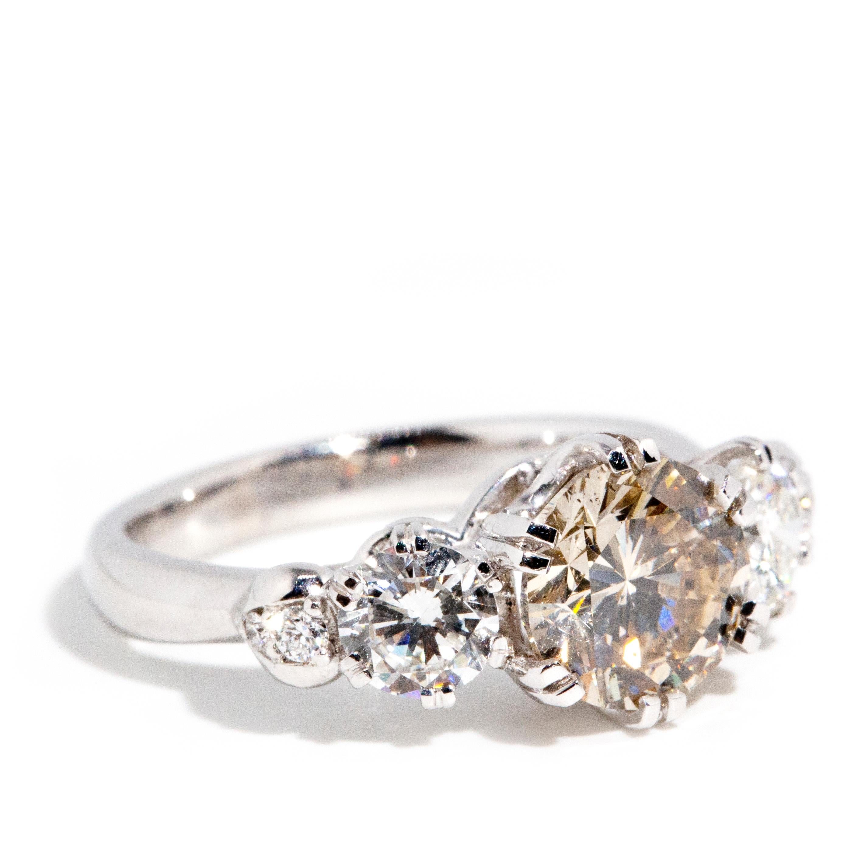 Forged in 18 carat white gold, this stunning contemporary ring features a stunning round brilliant diamond at the top of the band flanked by a fabulous duo of smaller round brilliant cut diamonds and additional diamonds around the setting. Her name