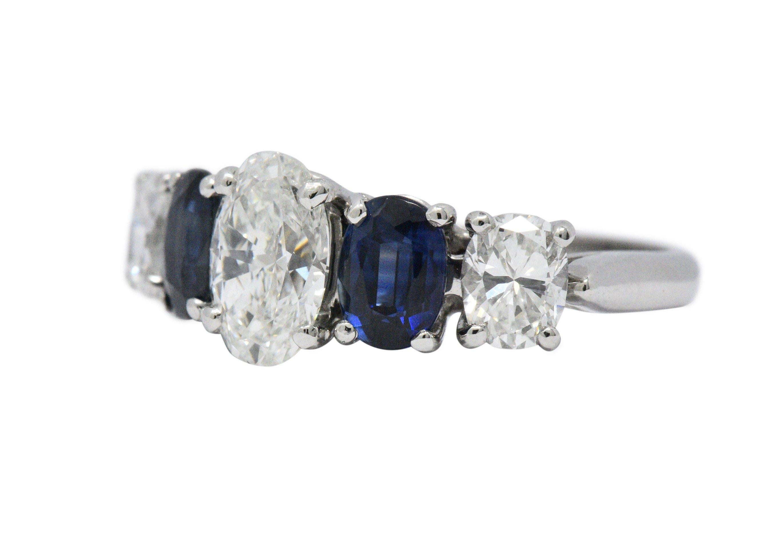 Centering an oval cut diamond weighing 1.00 carats, H color, VVS1 clarity and accompanied by a GIA Diamond Grading Report
Flanked by oval cut sapphires on each side, two total weighing approximately 1.20 carats total, deep blue and well matched
With