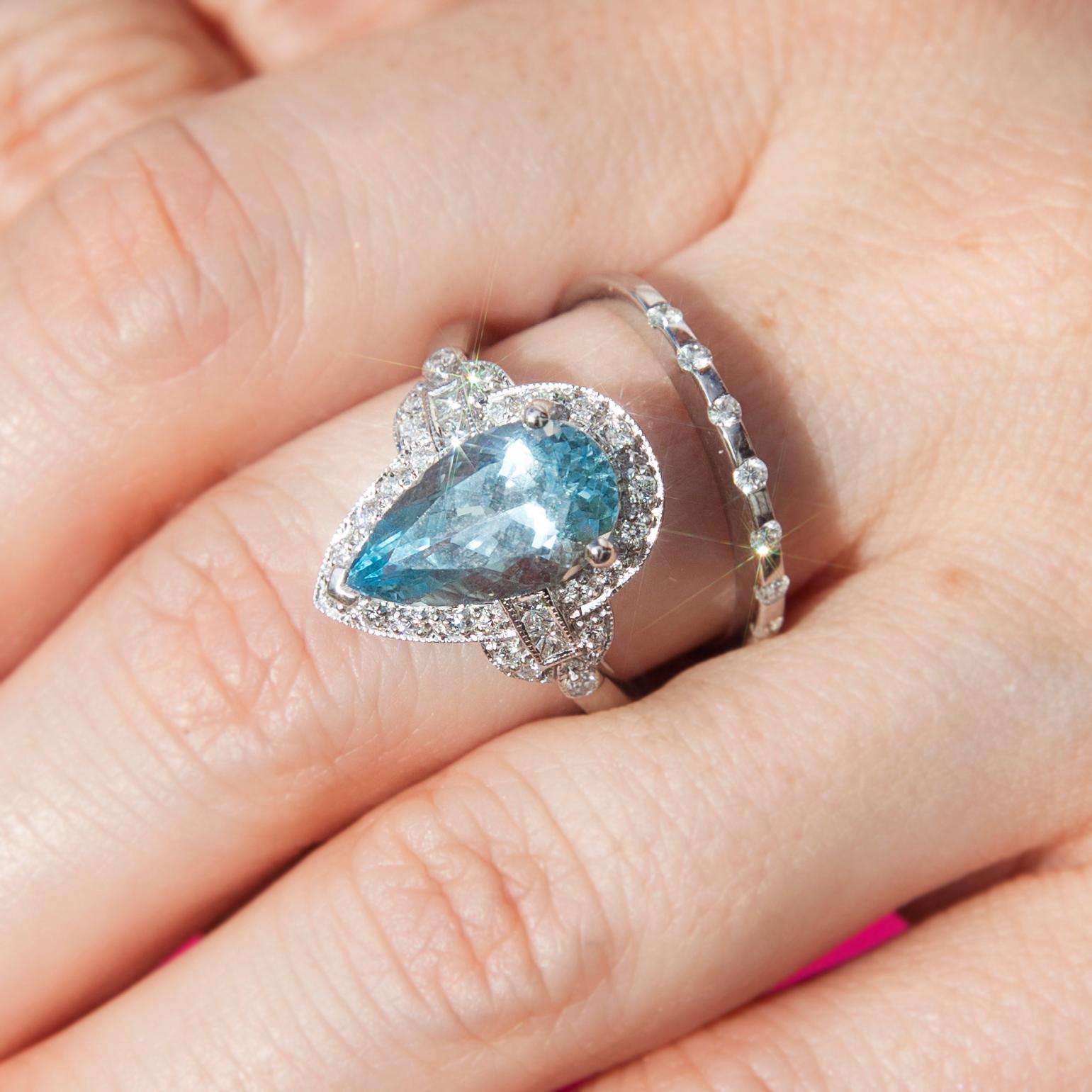 Crafted with love and care in 18 carat white gold, this fabulous art deco-inspired ring features a stunning pear-shaped faceted fine blue 2.95-carat aquamarine complemented by a captivating border of scintillating round brilliant cut diamonds