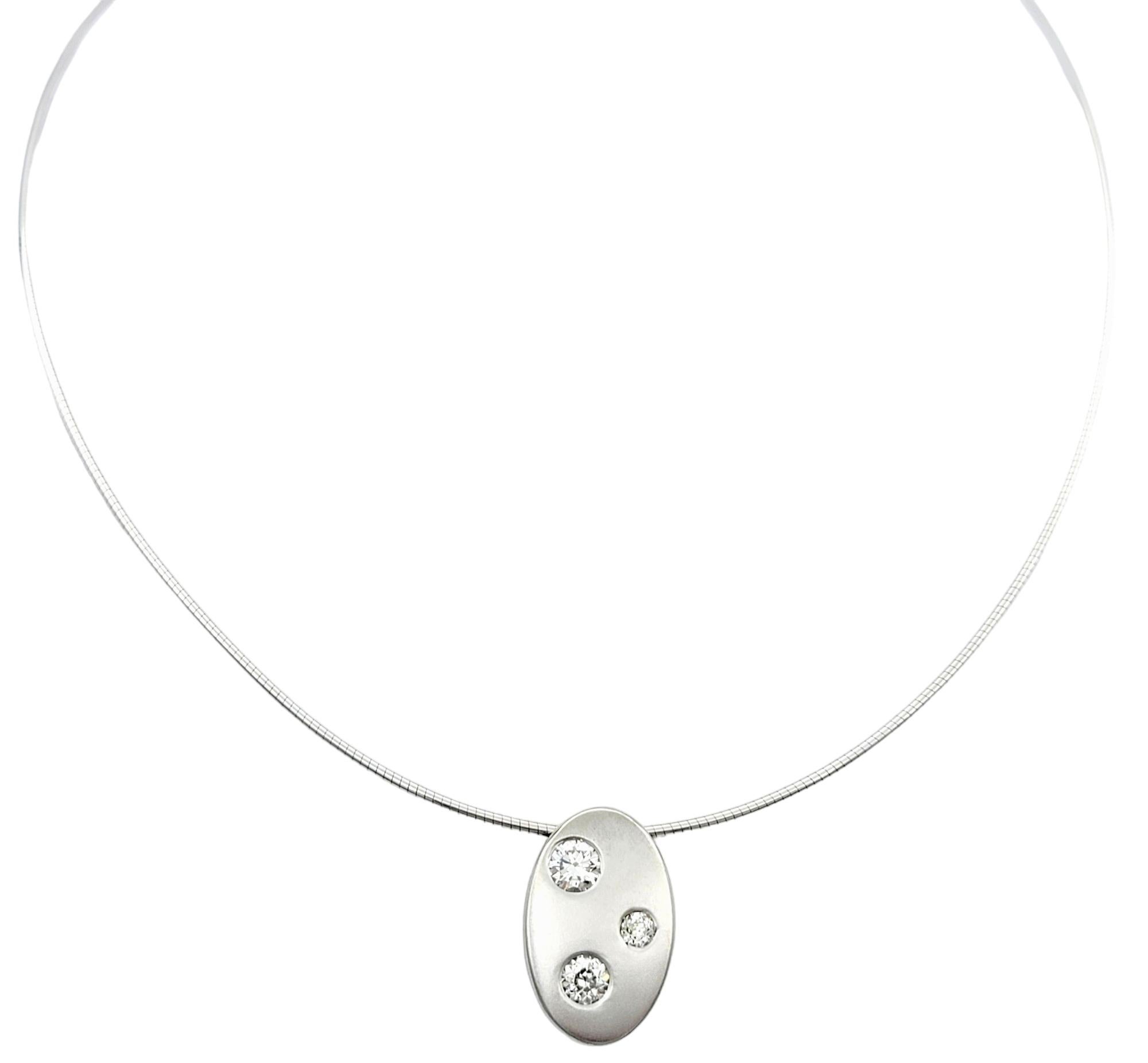 Questo splendido pendente moderno, disegnato ad arte con tre diamanti incastonati, è elegantemente sospeso su una catena a filo e incastonato in oro bianco 14 carati. Questo pezzo contemporaneo presenta un'elegante forma ovale, con i diamanti