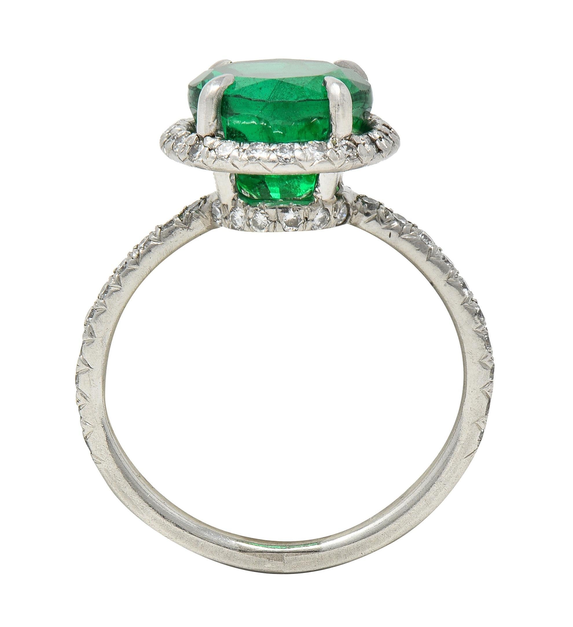 Centering a round cut emerald weighing 2.83 carats - transparent medium green
Natural Zambian in origin with minor traditional clarity enhancement - F2
Prong set in basket with a recessed round brilliant cut diamond halo surround
With additional