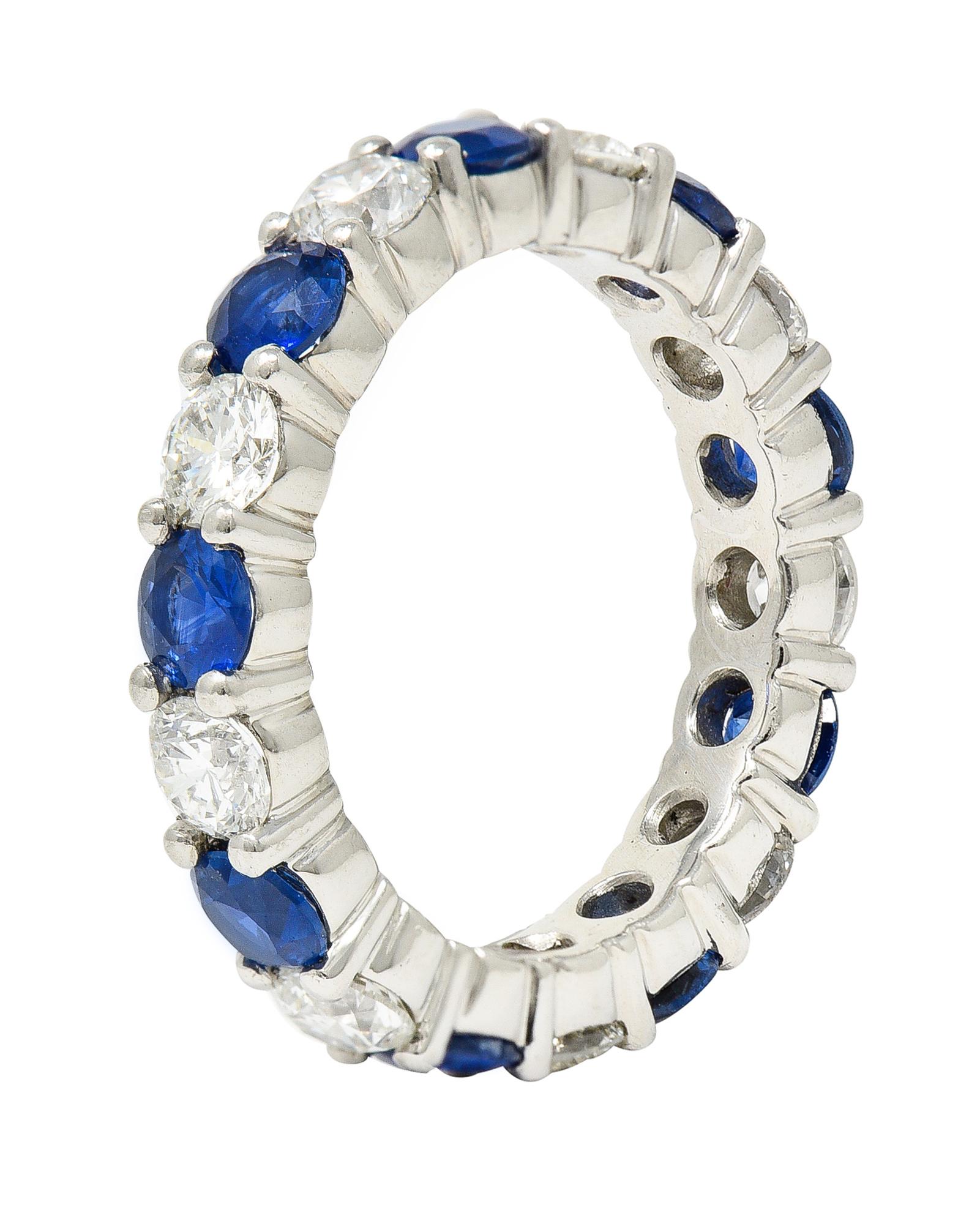 Eternity band ring features round brilliant cut diamonds alternating with round cut sapphires. Set via shared prong fully around. Total diamond weight is approximately 1.55 carat with I/J color and primarily SI1 clarity. Sapphires are well matched