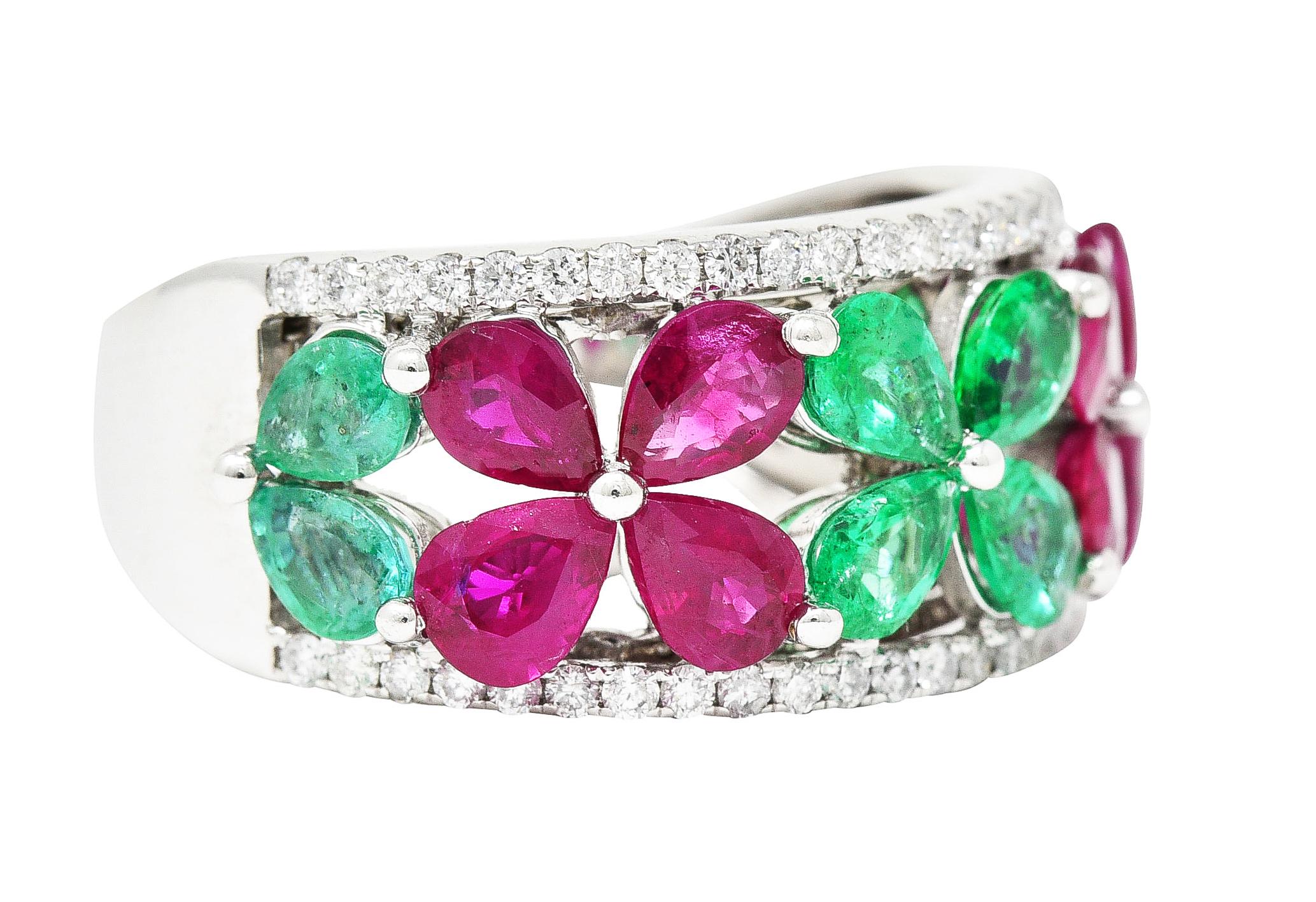 Wide band ring has a pierced center featuring a row of flowers comprised of pear cut gemstones. Emeralds are well matched while weighing in total approximately 1.85 carats - medium light bluish green. Rubies are well matched while weighing in total