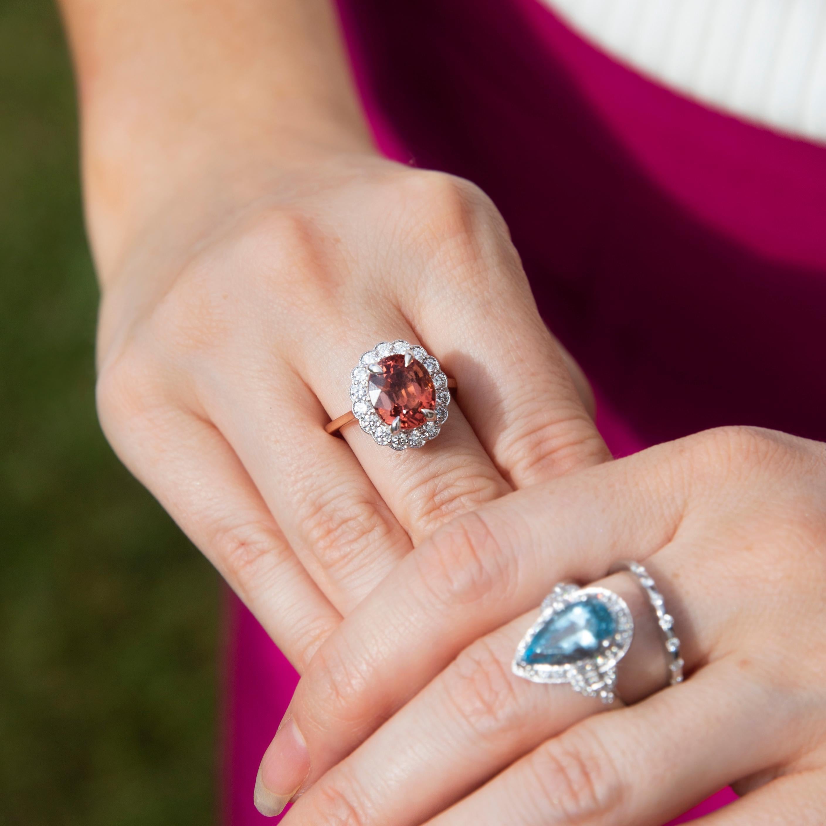 Réalisée avec amour en or rose et blanc 18 carats, cette superbe bague à halo est ornée d'une tourmaline ovale de 4,38 carats d'un rose orangé brillant et d'une bordure festonnée de diamants ronds de taille brillant. Nous avons baptisé cette