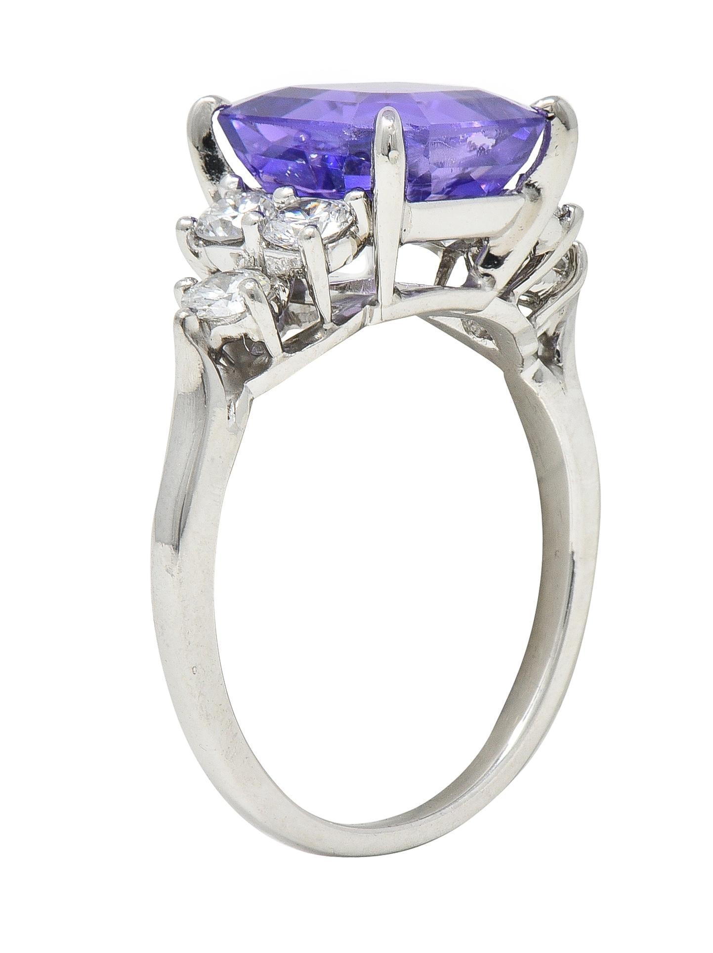 Centering an emerald cut sapphire weighing 4.15 carats - transparent medium purple in color
Natural Sri Lankan in origin with no indications of heat treatment 
Prong set in basket and flanked by clusters of round brilliant cut diamonds 
Weighing