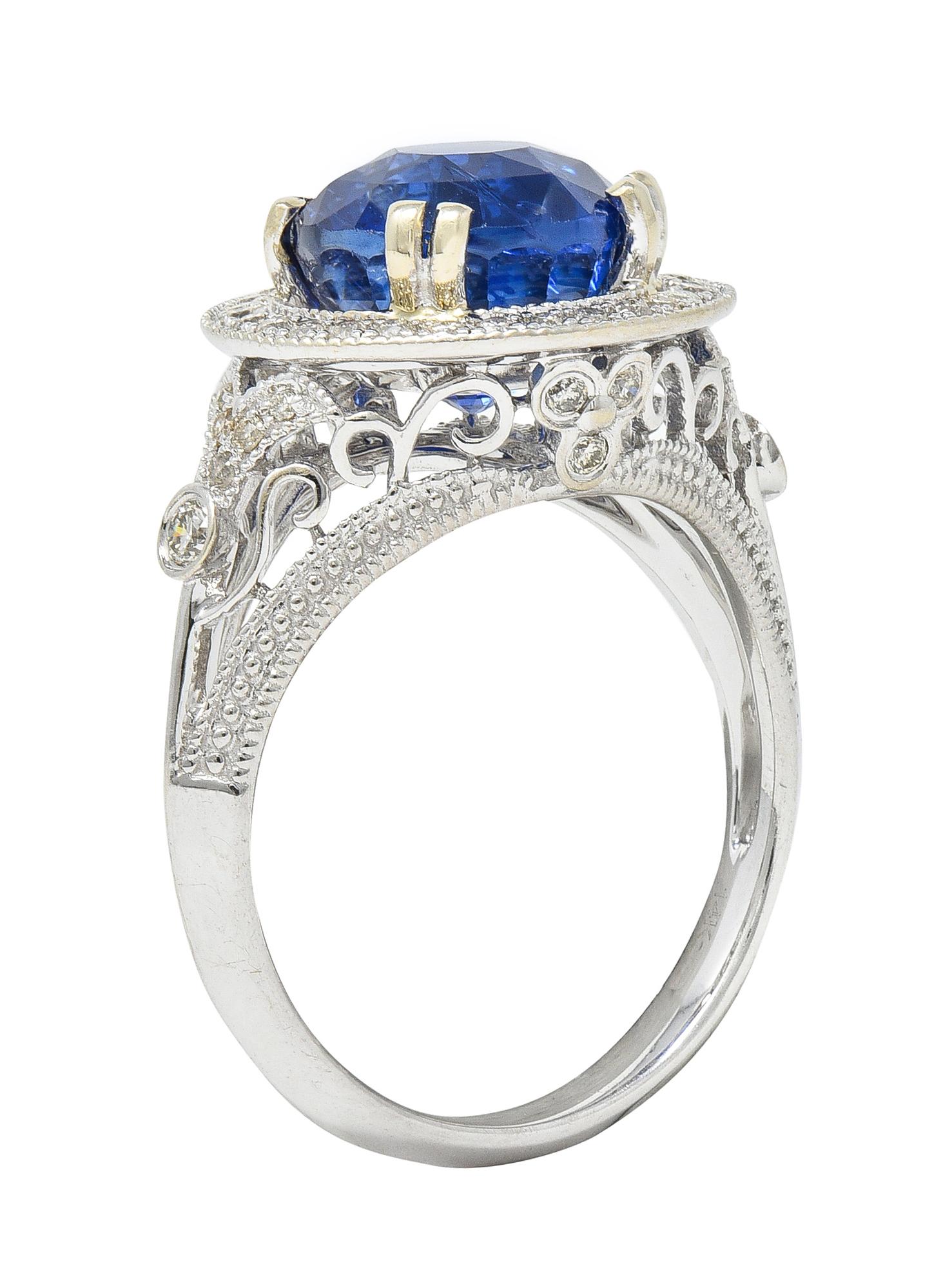 Centering a round cut sapphire weighing 4.48 carats - transparent medium blue in color 
Prong set with a recessed halo surrounded by round brilliant cut diamonds
With additional diamonds in pierced scroll and floral motif surround
Weighing