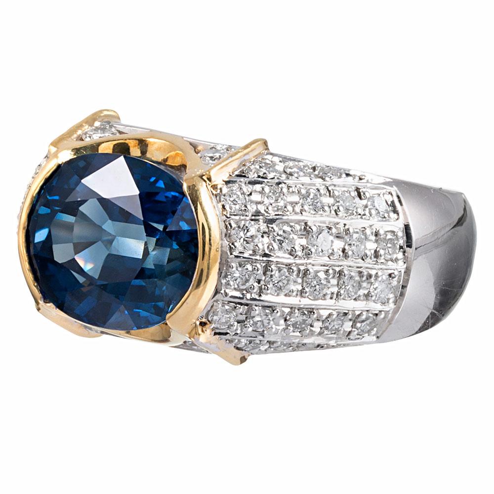 A contemporary design rendered in platinum with 18 karat yellow gold accents, the center piece is a 5.52 carat faceted oval sapphire, set “East-to-West” with .80 carats of diamond accents decorating the shoulders. The smooth sides make this ring sit