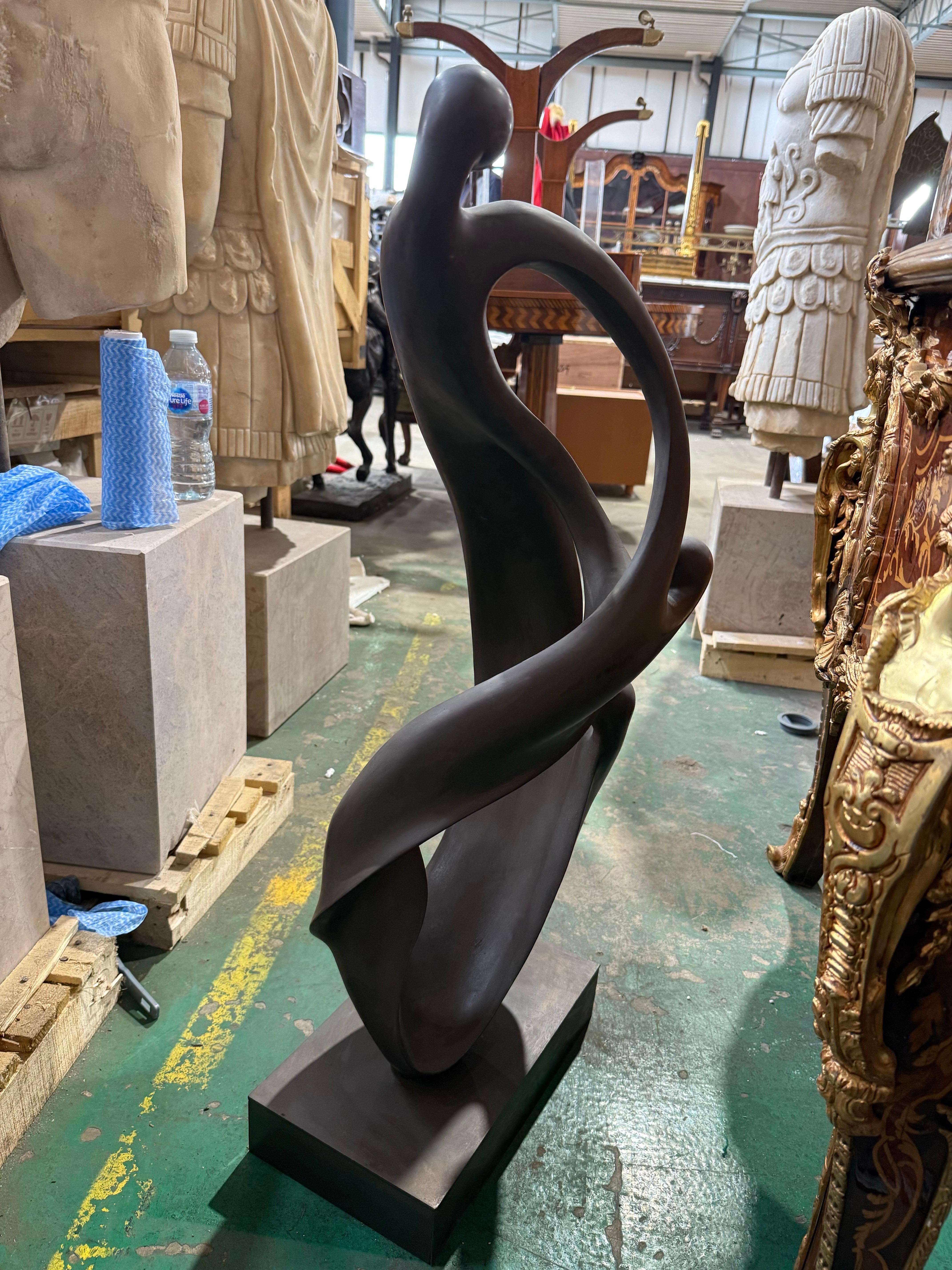 Una escultura abstracta contemporánea de bronce, elegante y fluida, titulada sugerentemente Unidad en movimiento, que representa tres figuras estilizadas que se entrelazan con gracia en una forma continua y fluida. Con una silueta rítmica y
