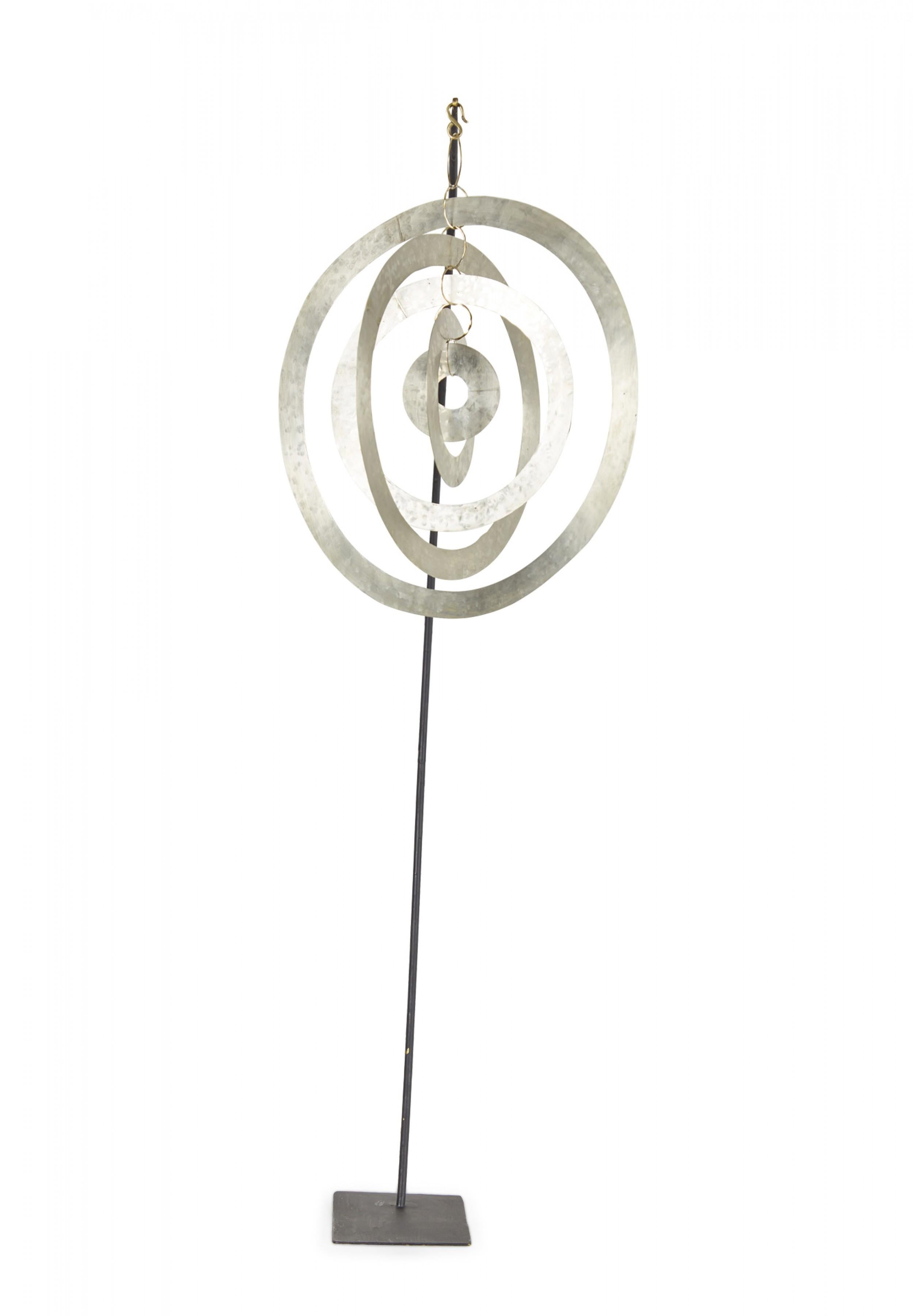 Contemporary sculpture /mobile featuring concentric hammered nickel circles and ovals suspended on a curved black metal stand titled, 