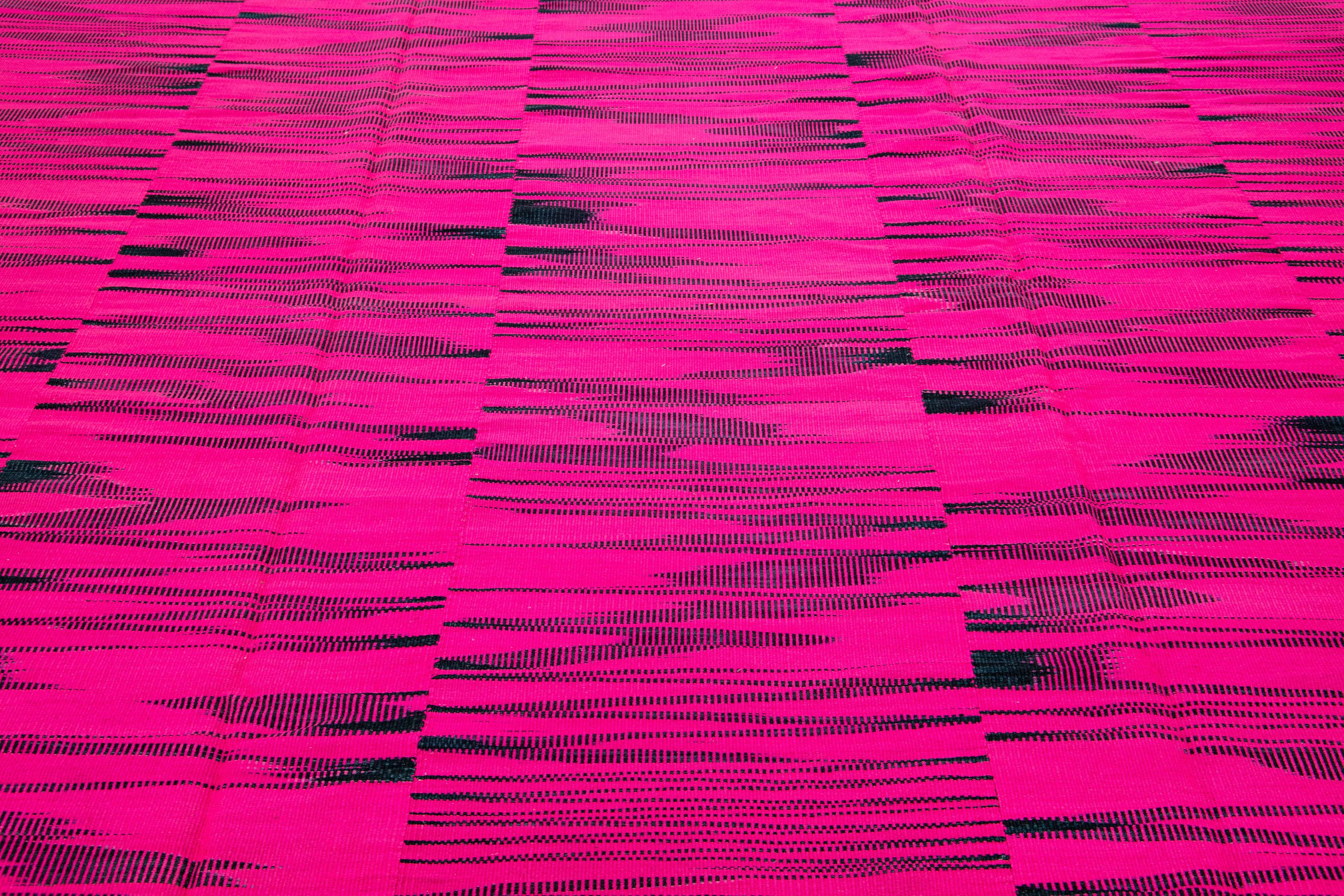 This contemporary Turkish kilim rug, crafted in the 21st century, features a vibrant highlighter-pink field adorned with an all-over abstract geometric design composed of interlocking black stripes.

This rug measures 11'4