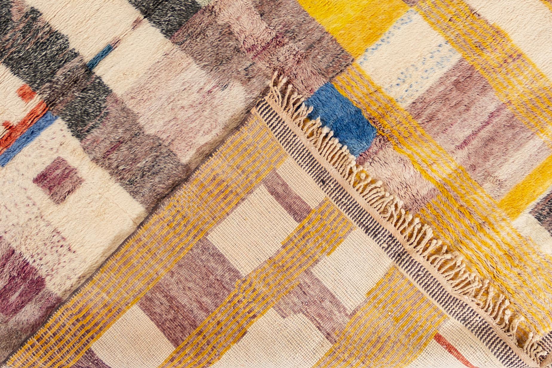 A contemporary Moroccan rug with an ivory field and yellow, red and blue geometric shapes in an all-over abstract design. This rug has a luxuriously thick hand knotted wool pile and measures 11'3