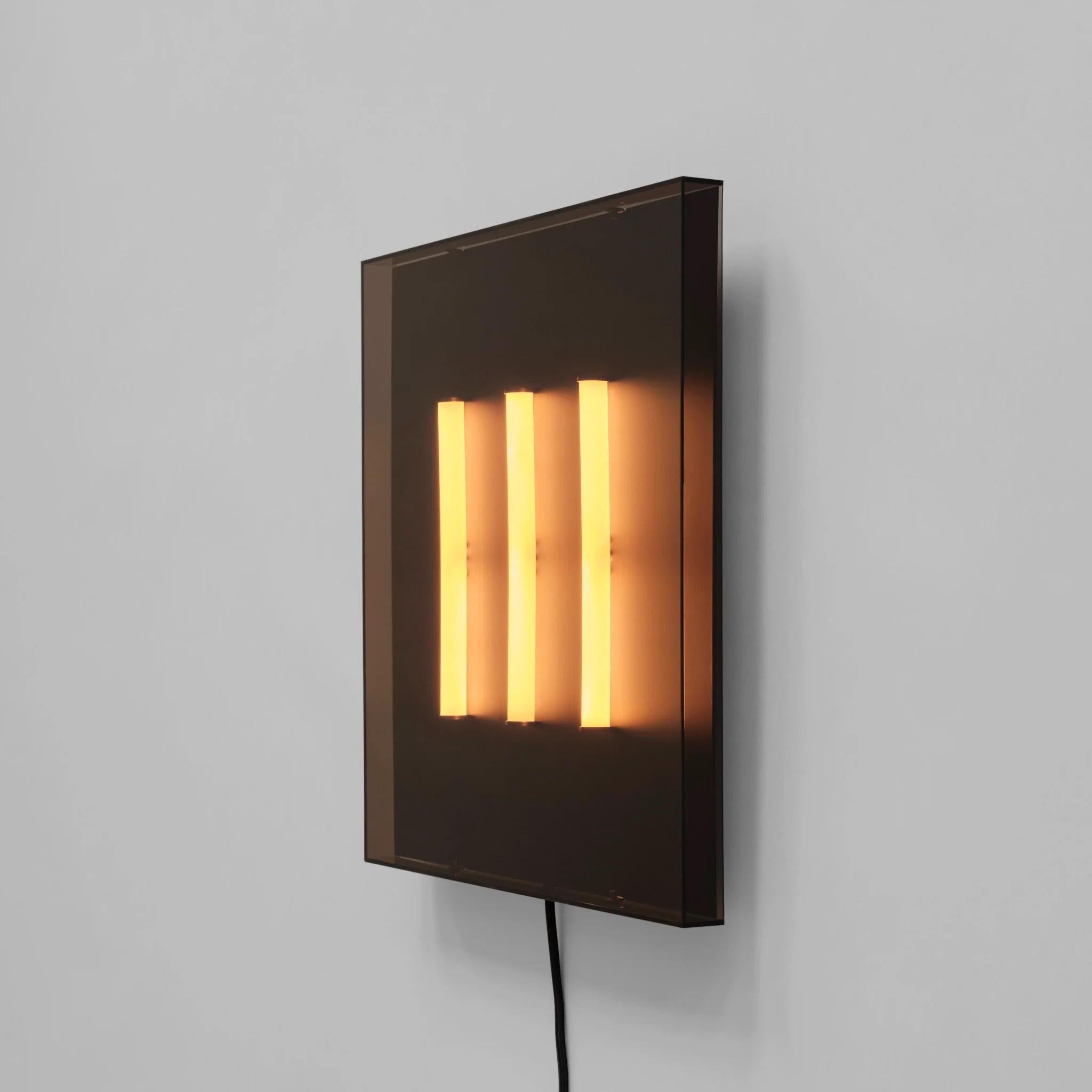 Applique contemporaine en acrylique et métal.
 
Cette lampe murale s'inspire de l'esthétique des néons des années 1980. Composé d'un abat-jour carré en acrylique dans une teinte taupe semi-transparente, trois tubes rayonnants créent un motif