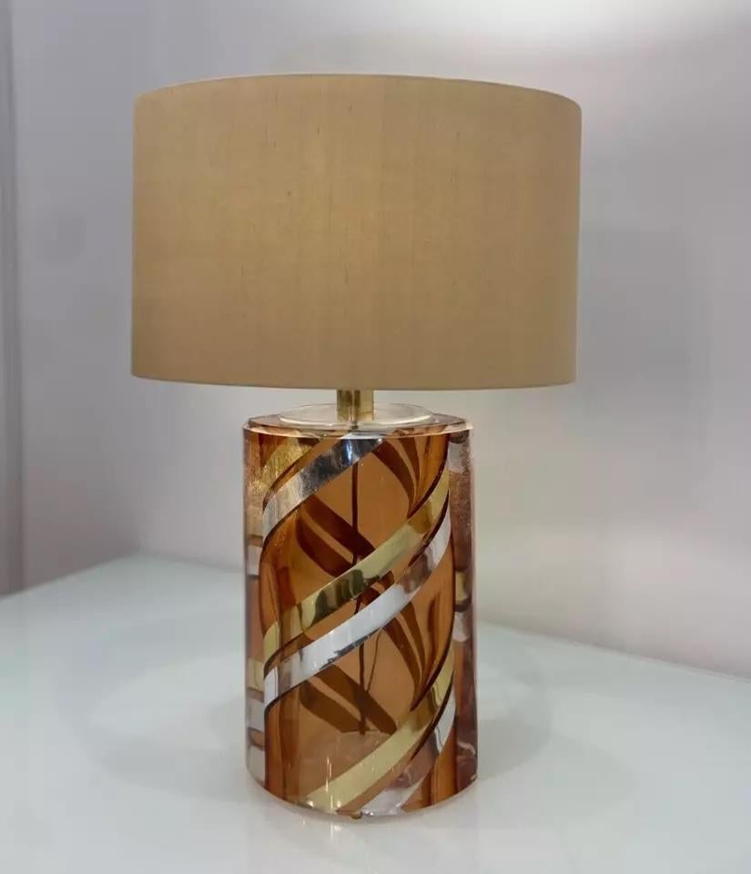 Eine moderne Tischleuchte aus bernsteinfarbenem Glas mit spiralförmigem Design in Gold und Silber und einem beigen Leinenschirm. 

Aus hochwertigem MATERIAL gefertigt, spiegelt sich dies im Gewicht der Lampe wider. 

Beide Seiten des Leuchtenfußes