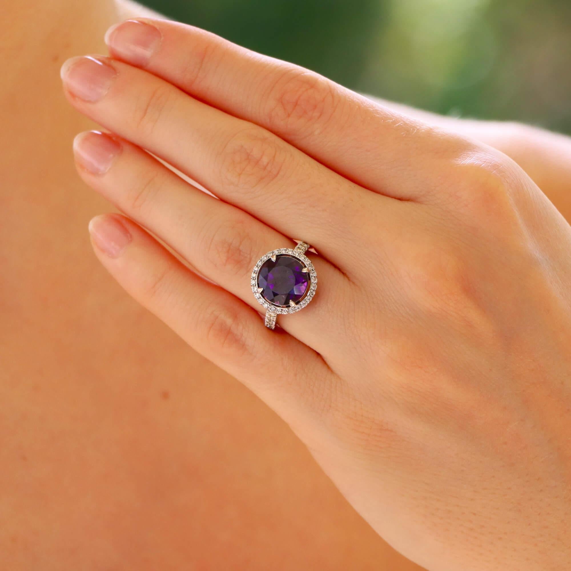 A beautiful amethyst and diamond halo ring set in platinum.

The ring centrally features a beautiful purple round cut amethyst surrounded by a halo of 28 round brilliant-cut diamonds. Each shoulder is further accented with 5 round brilliant cut