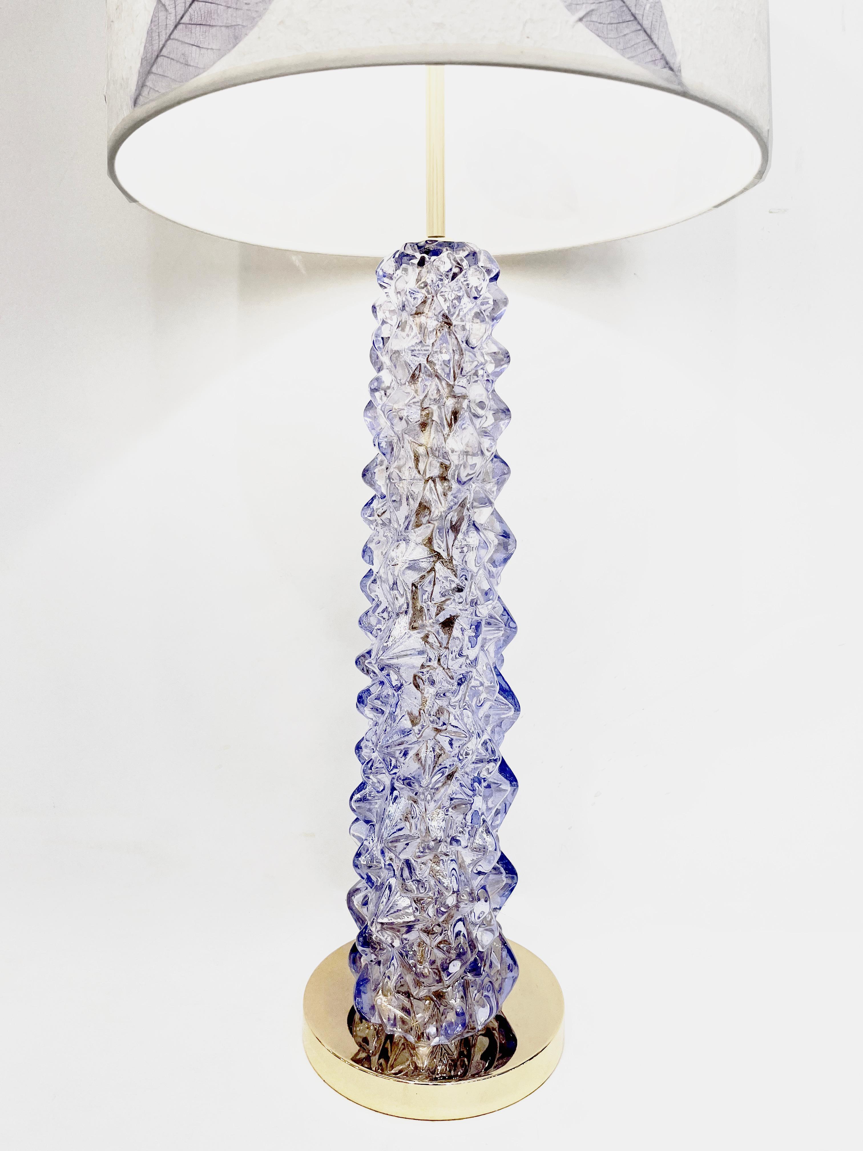 Modern Italian pair of tall lamps in Murano glass in a glowing lavender violet color, the central body worked with an irregular diamond-cut jewel-like texture that multiplies light reflections and play of color, raised on a polished brass round