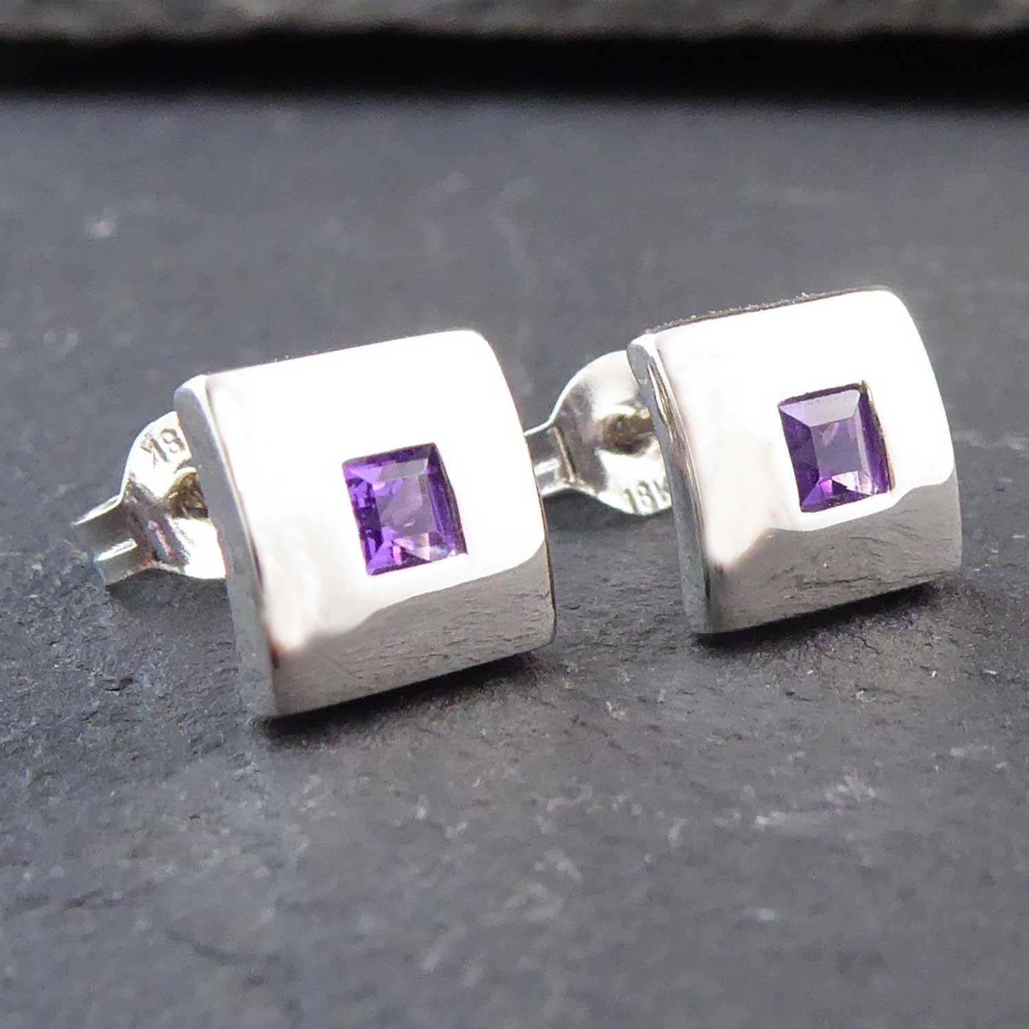 Modern, pre-owned amethyst stud earrings, each earring featuring to the centre a square cut amethyst of dark pinkish purple hue.  White polished square surround, sightly bevelled to sit neatly on the earlobe.  White post and butterfly fittings for