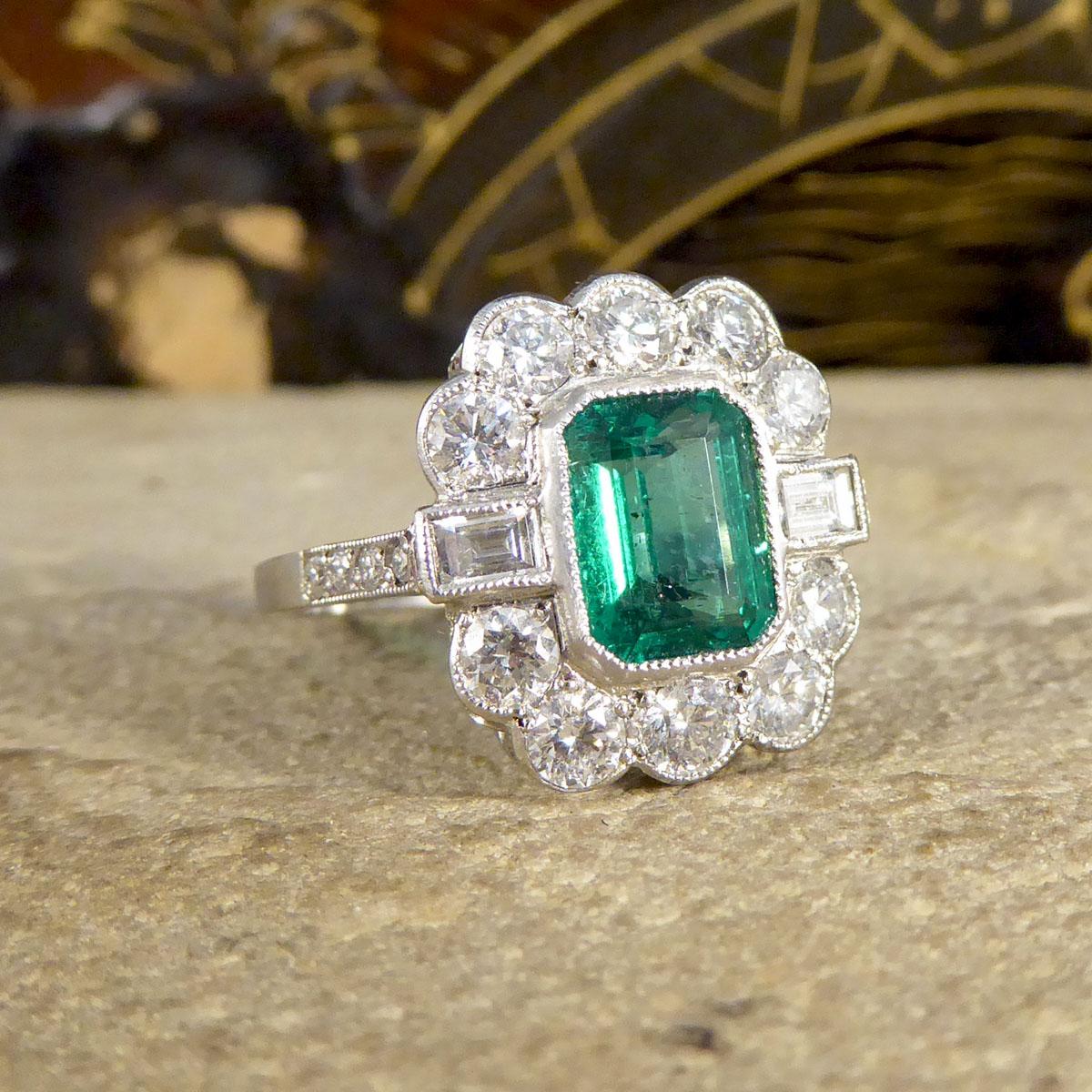 This gorgeous 1.62ct emerald cut Emerald is surrounded by 10 brilliant cut diamonds along the top and bottom of the Emerald and two baguette cut Diamonds to either side creating a cluster. With small Diamonds adorning the shoulders of this ring