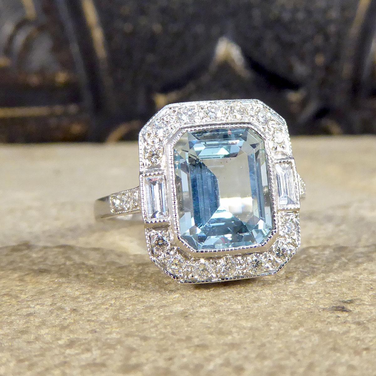 This statement cluster ring holds a 2.10ct Emerald Cut Aquamarine in a rub over collar setting with a Diamond surround. With a total Diamond weight of 0.45ct, these modern brilliant cut and baguette cut diamonds create an extra sparkle to this