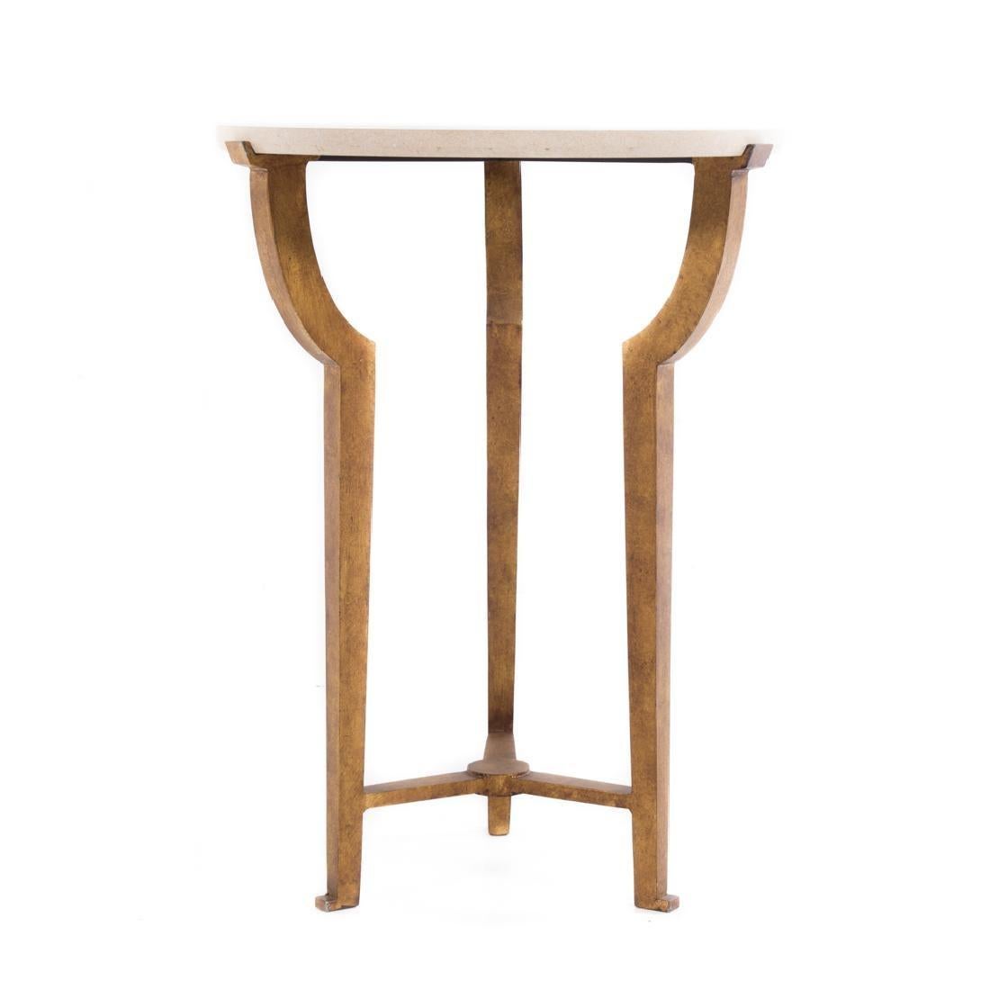 A round side table with a travertine top rests on a trefoil iron gilt base. The base supports bow out at the top in a trefoil design, and then taper into straight legs with pad feet. A center support anchors the table at the bottom. The dimensions