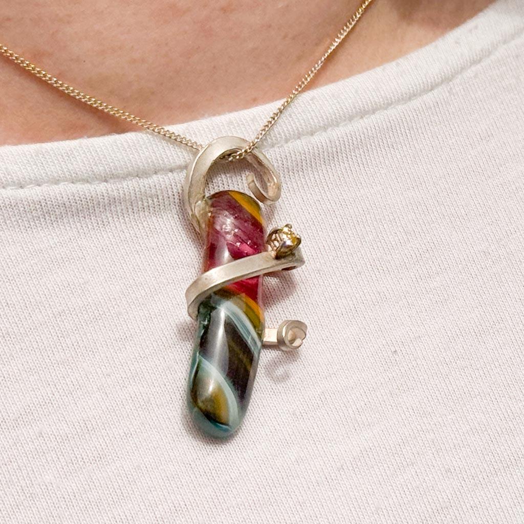 Award-winning Tara Lois was influenced by the Art Nouveau style when she designed this contemporary organic pendent. The abstract curves have been handcrafted from sustainable satin finished sterling / 925 silver fused to Maltese glass and