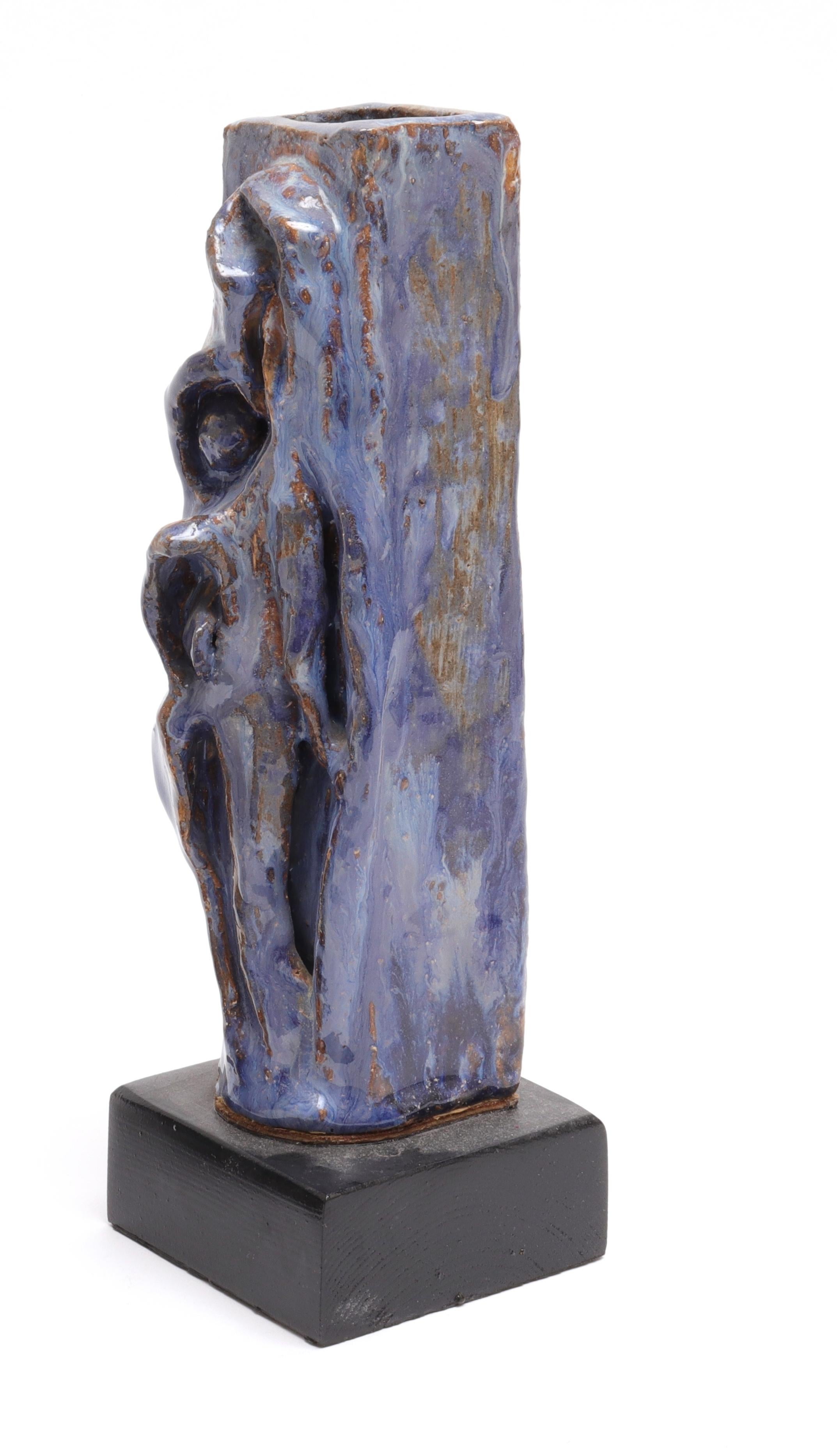 Vase en poterie d'art contemporain à glaçure bleu-vert, forme rectangulaire haute avec décoration sculptée de figures stylisées, monté sur une base en bois.