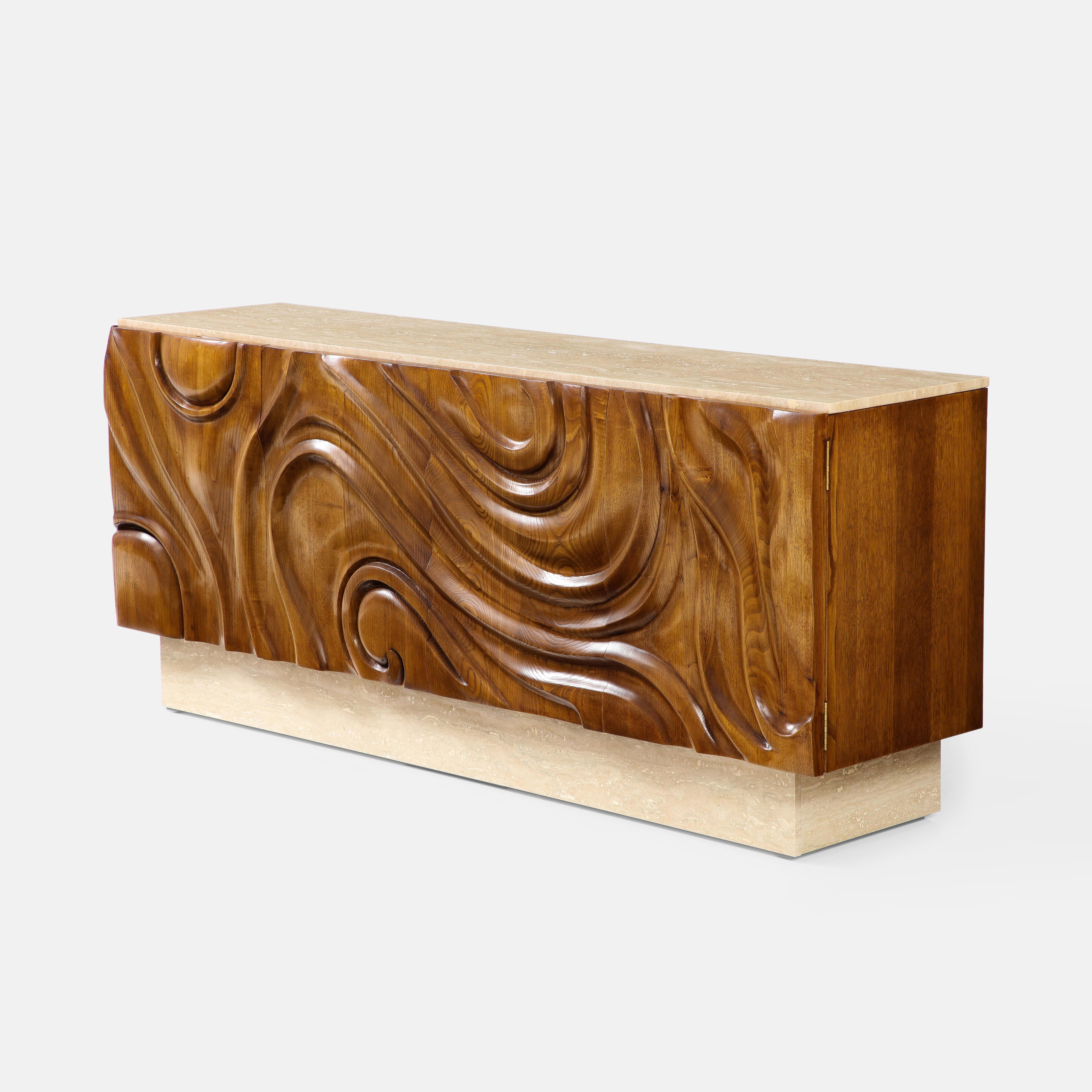 Contemporary Italian artisan four-door carved oak cabinet in the Modernist style with travertine top and plinth.  This exquisite handmade cabinet consists of sculptural hand-carved oak door panels in a stylized organic swirl pattern creating