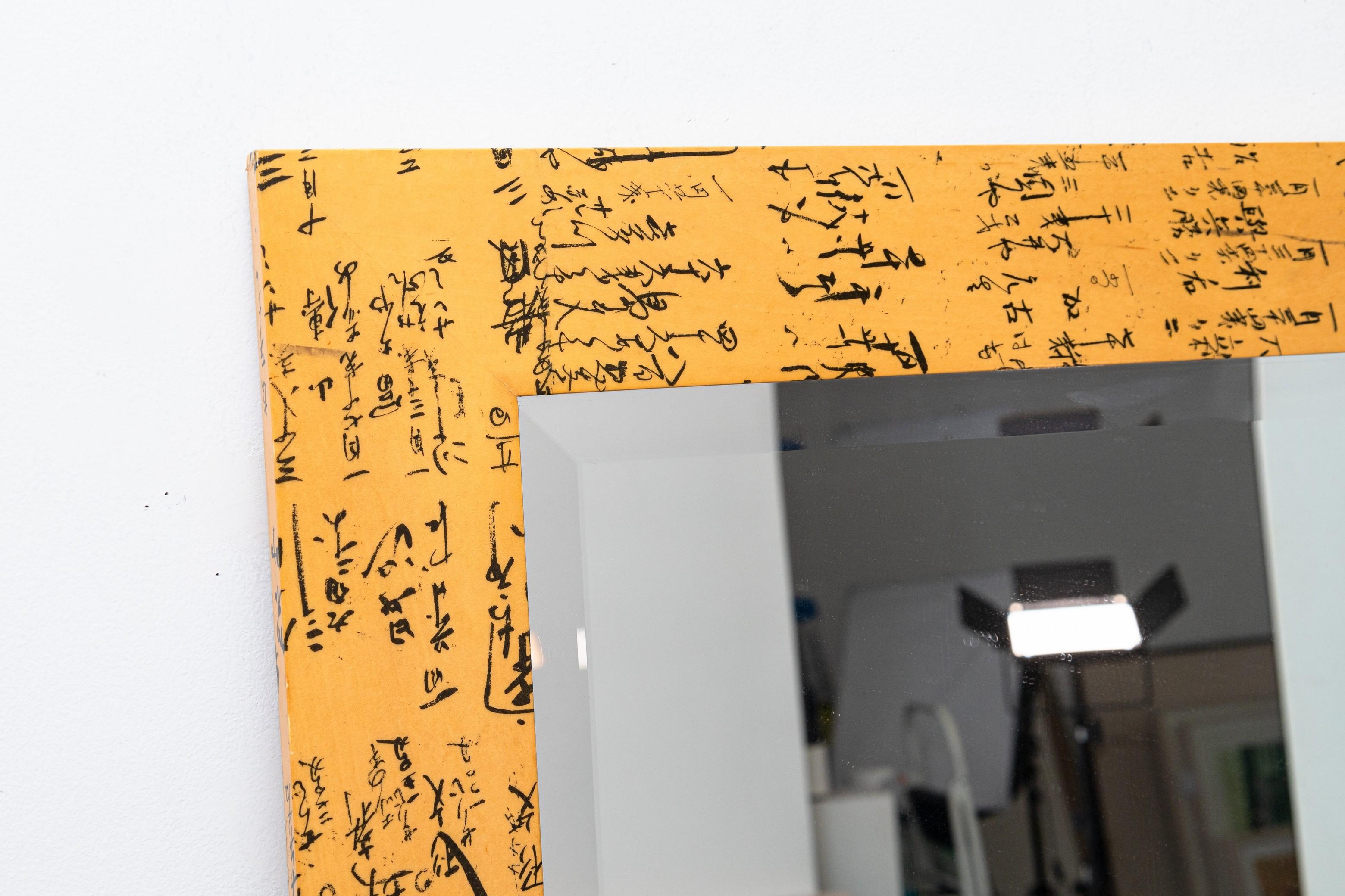 A Century Furniture Washi Script mirror. This lovely large mirror features an Asian script design stretching across the frame of the mirror. The black text sits on a tan/yellow/orange colored frame. The mirror itself is a crystal clear rectangular