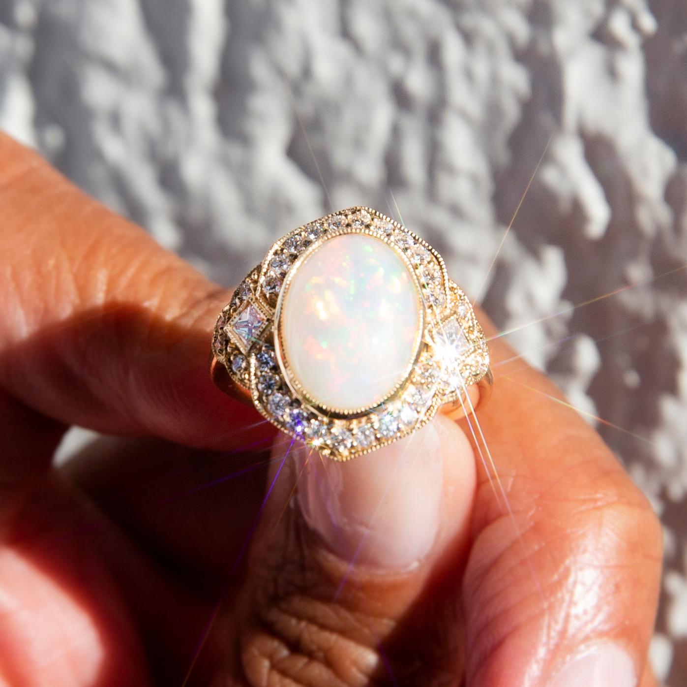 Lovingly crafted in 18 carat gold, this stunning art-deco-inspired contemporary ring has a captivating oval Australian crystal opal at her centre afire with bright flashes of orange, green, and red play of colour. This fabulous gemstone rests in a