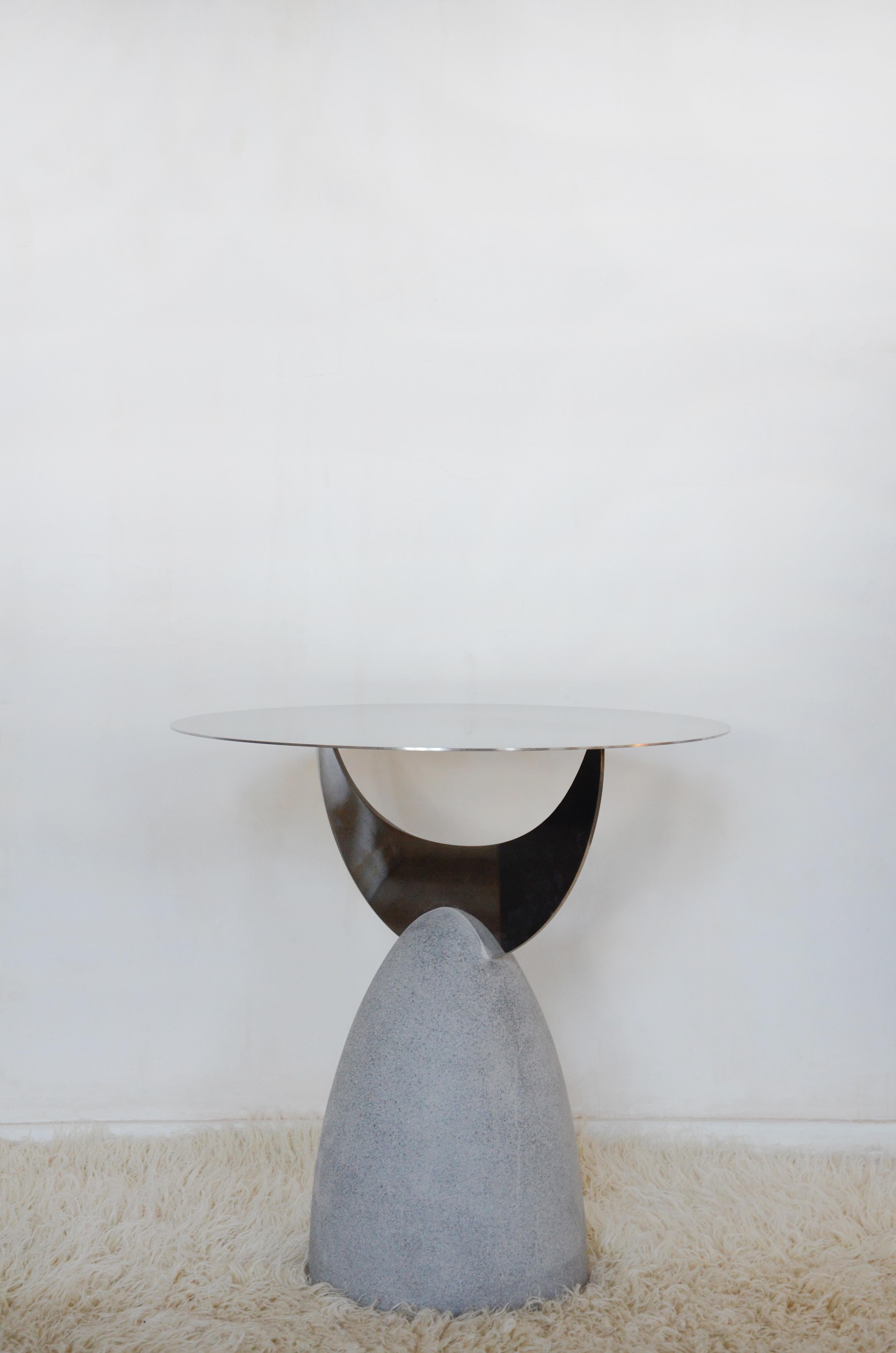 This unique, sculptural metal and stone side table is expertly hand-crafted and designed by Rooms Studio in Tbilisi, Georgia. The piece features a circular mirror-finish stainless steel top, positioned atop a stainless steel crescent moon, with a