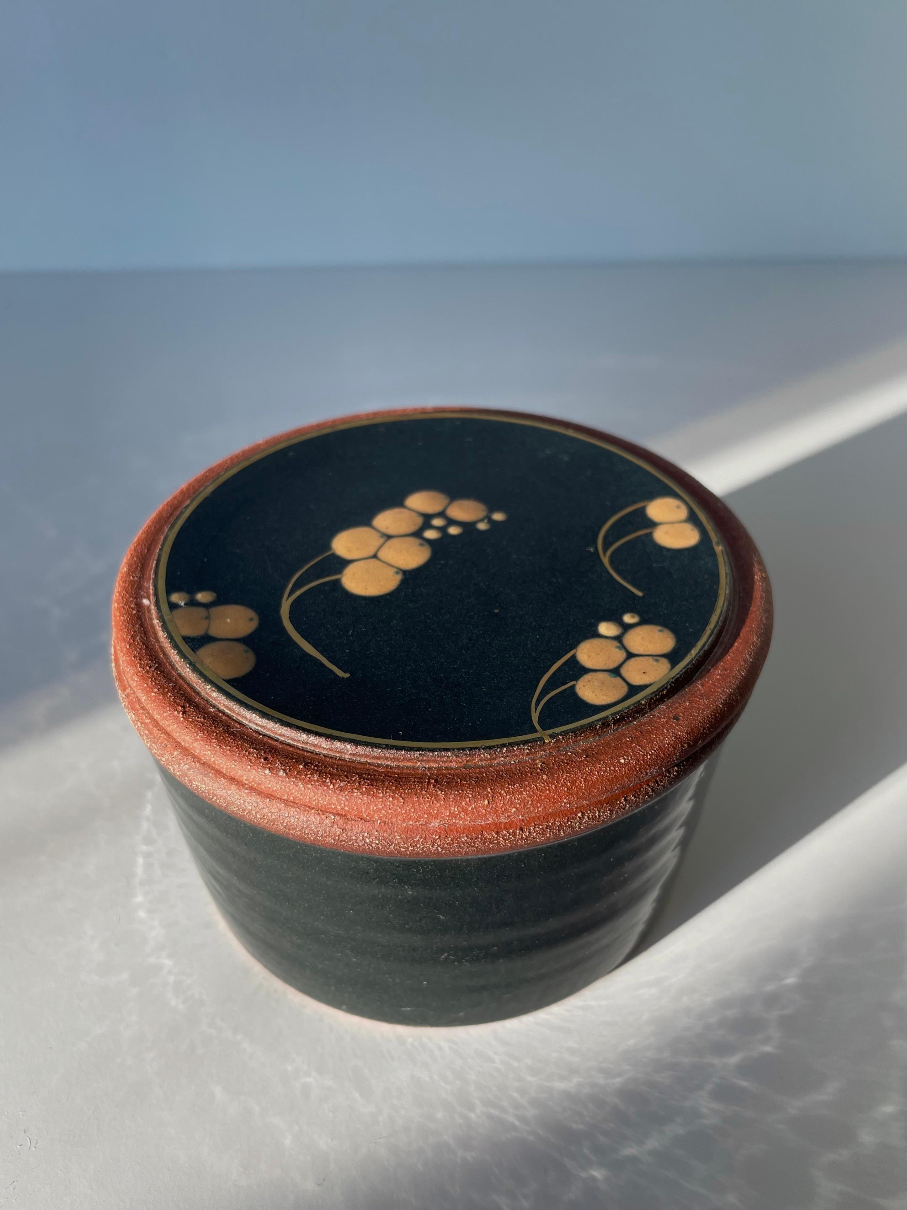 Hand-thrown modern ceramic lidded bonbonniére jar by Danish artist Ulla Sonne on the Danish island of Funen in the 2010s. Shiny black glaze with unglazed edges and base. Peach colored stylized organic decorations on lid. Signed under base. Beautiful
