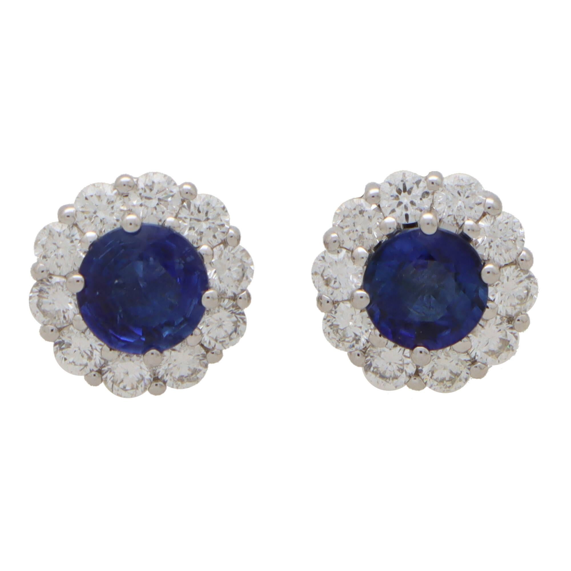 An elegant pair of blue sapphire and diamond cluster stud earrings set in 18k white gold.

Each earring depicts a floral cluster motif centrally set with a deep vibrant blue sapphire and surrounded by 10 round brilliant cut diamonds. The earrings
