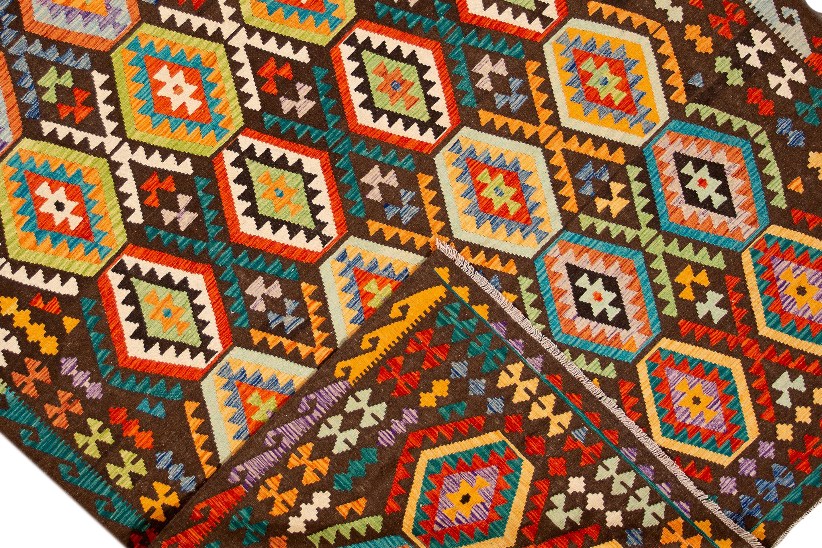 Dieser moderne, handgefertigte Kilim-Wollteppich zeichnet sich durch ein sattes braunes Feld aus, das mit einem lebhaften, mehrfarbigen geometrischen böhmischen Muster verziert ist.

Dieser Teppich misst 8'3