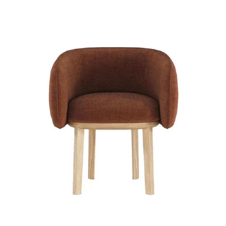 This dining chair features a subtle yet striking sculptural design. Its gentle curves and shape provide a cozy, nest-like feel, inviting relaxation and comfort. The chair rests on a distinctive base that echoes the shape of a sword, expertly crafted