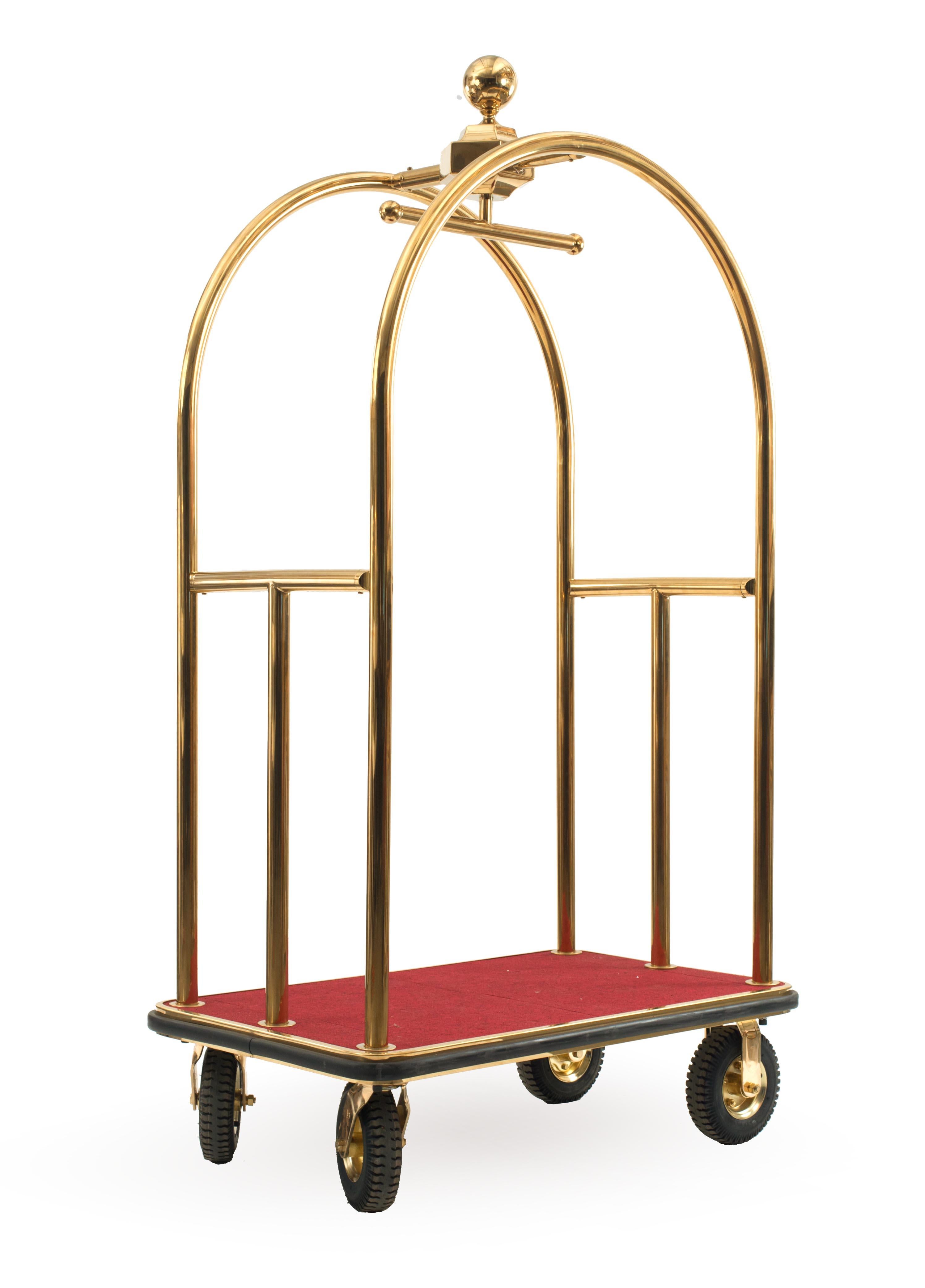 Contemporary brass hotel luggage rack / cart with a red carpeted platform and four swiveling rubber wheels.
  