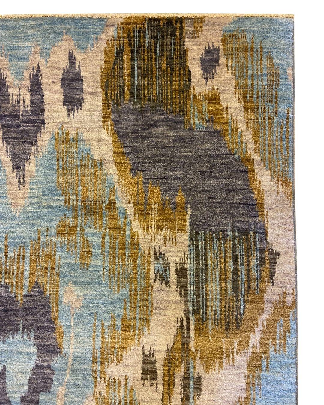 Ce tapis contemporain en laine Ikat indien aux couleurs bleu, or, gris et crème, mesurant 4' x 6', transforme une tradition textile vieille de plusieurs siècles en une déclaration moderne et vibrante. Son design audacieux et pictural reprend les