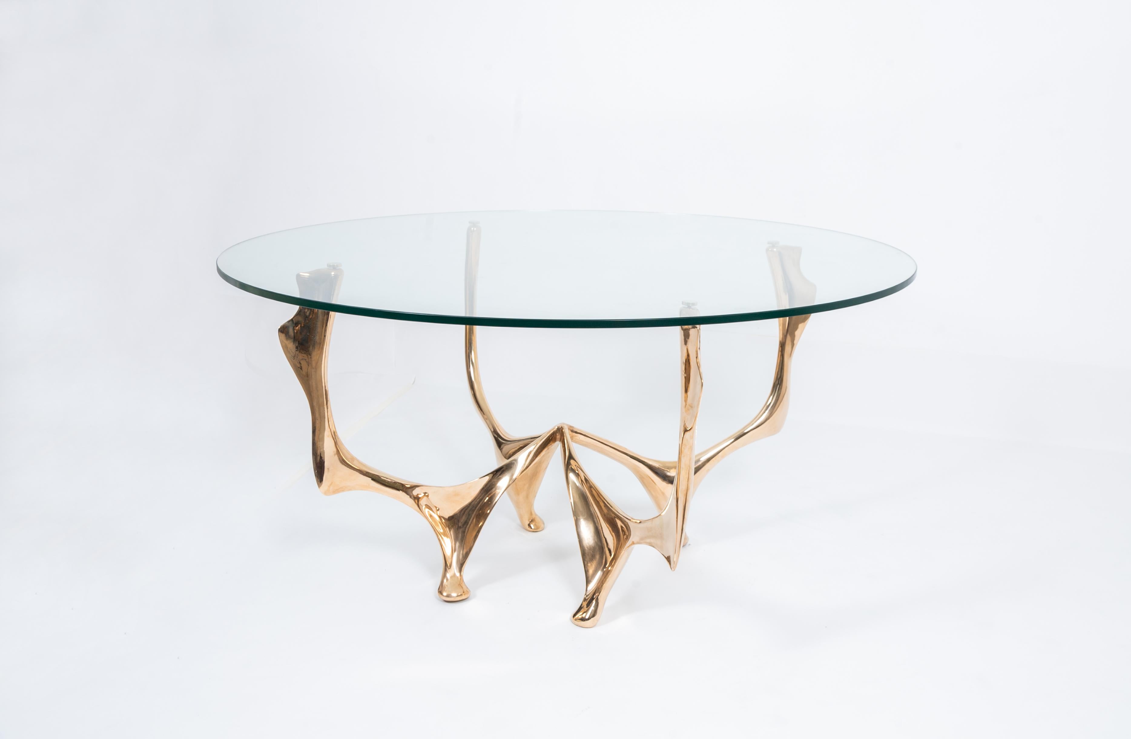 Elan Dining Table by Pierre Salagnac 
Material: Bronze golden polish, glass top
Dimensions: H 74 x Ø 150 cm
Year: 2023
Limited edition: numbered 1/8, signed

Revealing the organic curves of nature in the metal block with great talent, Pierre
