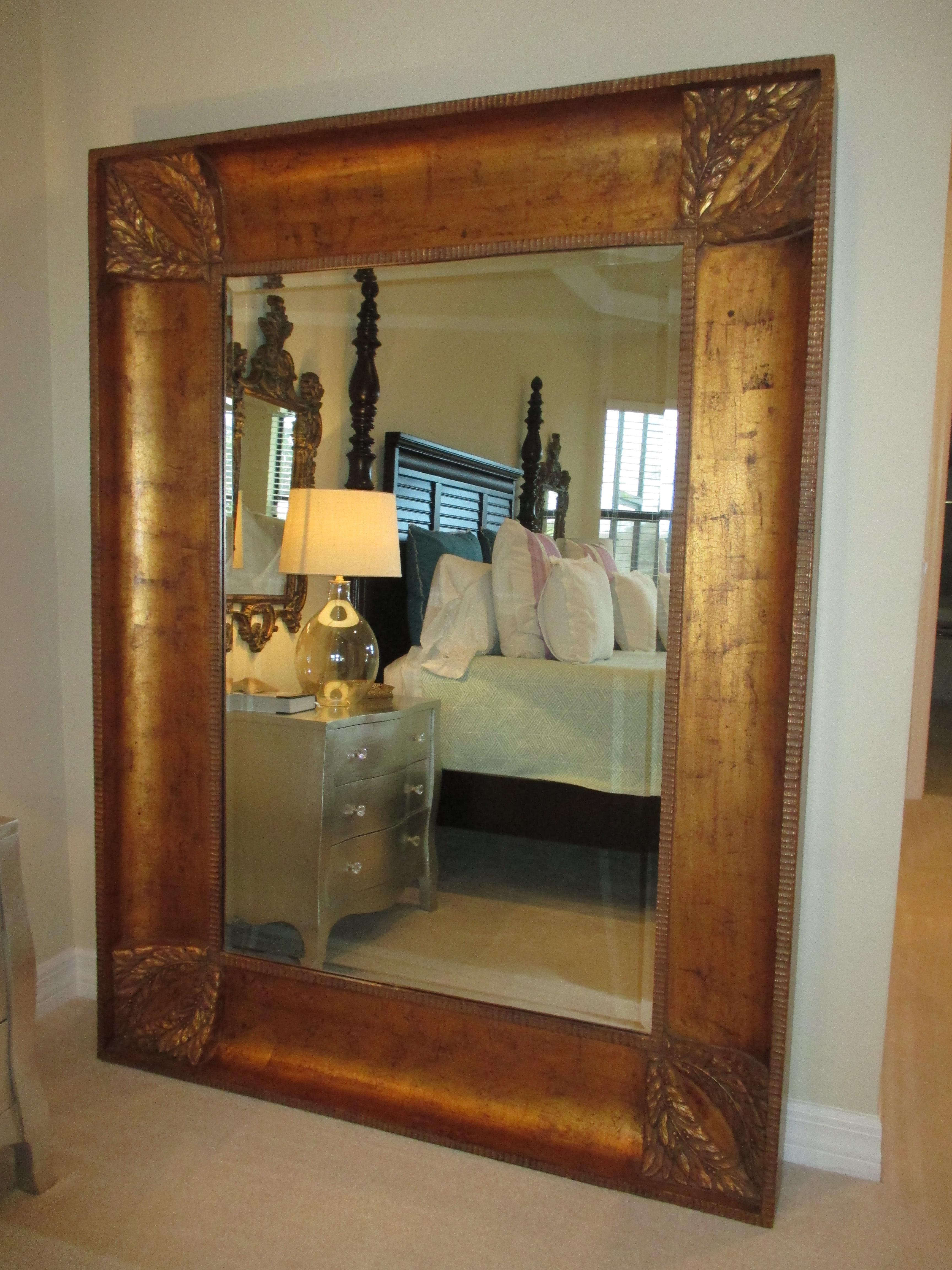 Beveled floor mirror featuring a wood frame with carved leaves and berries on each corner and a bronze finish. Hardware on back.