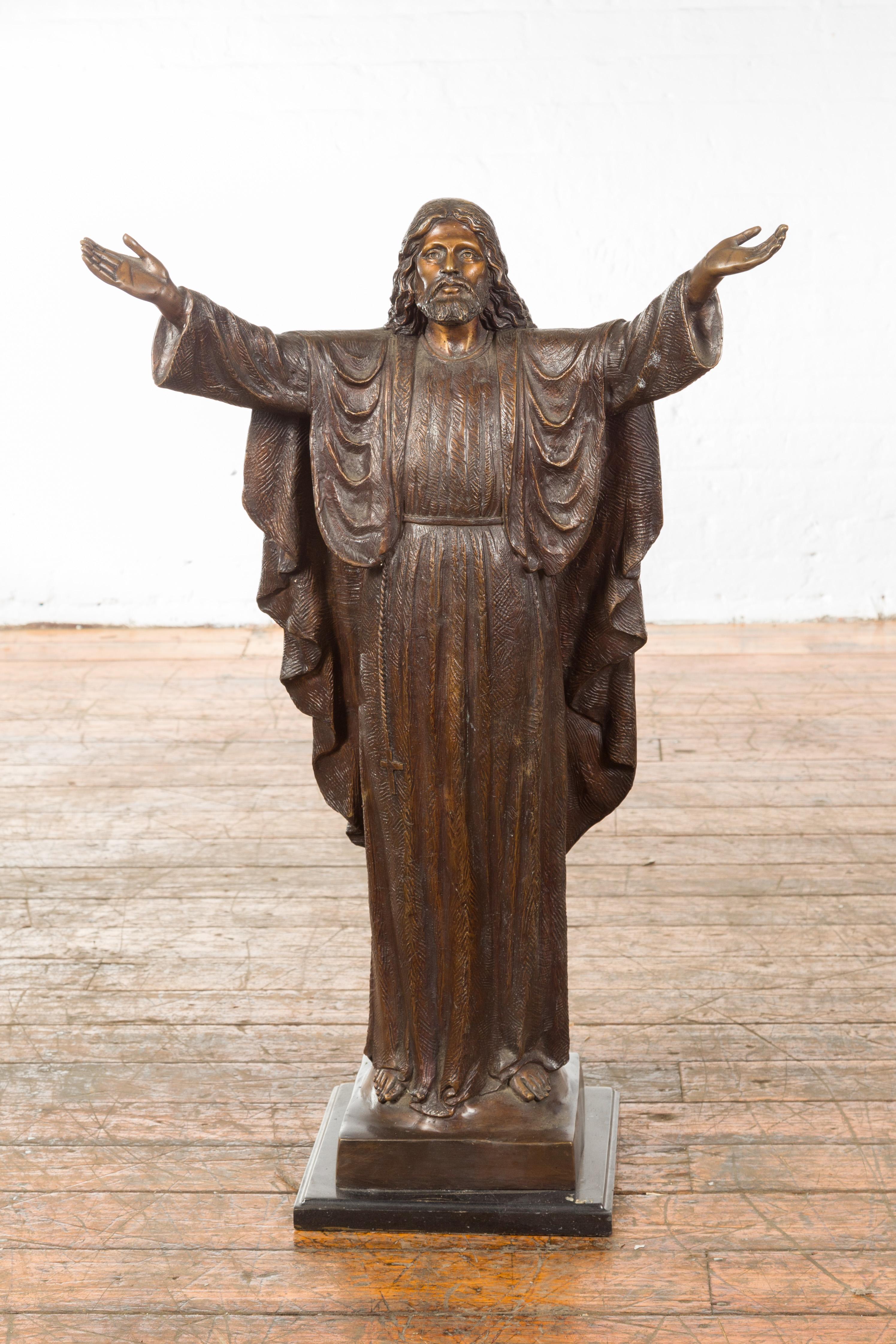 A small contemporary bronze lost wax statue of Jesus Christ with open arms, mounted on a square base. Created with the traditional technique of the lost-wax (à la cire Perdue) that allows a great precision in the details, this bronze statue depicts