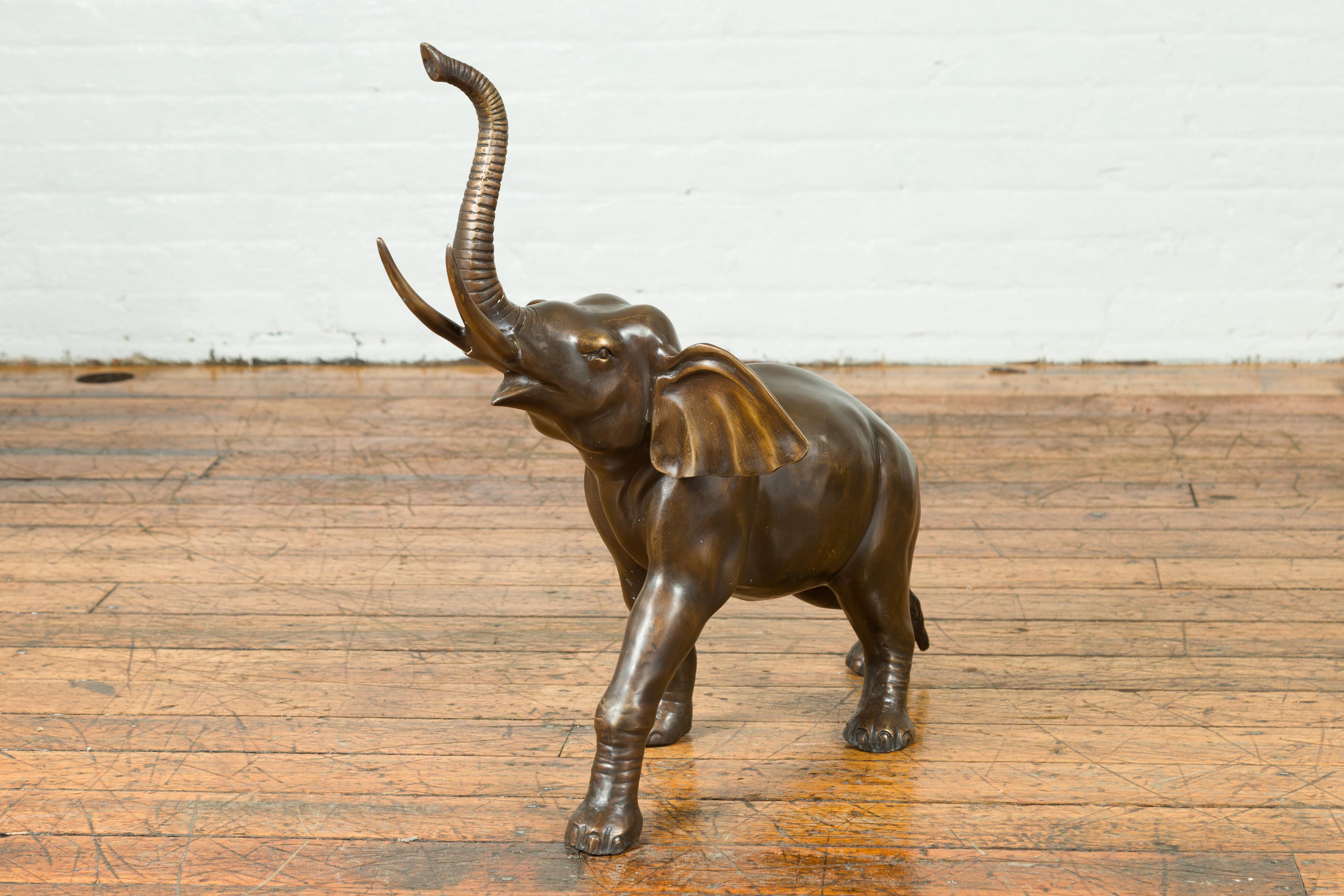 Sculpture contemporaine en bronze représentant un éléphant marchant, la trompe levée. Nous avons une paire disponible, avec les éléphants respectivement tournés vers la gauche et la droite. Créée selon la technique traditionnelle de la cire perdue