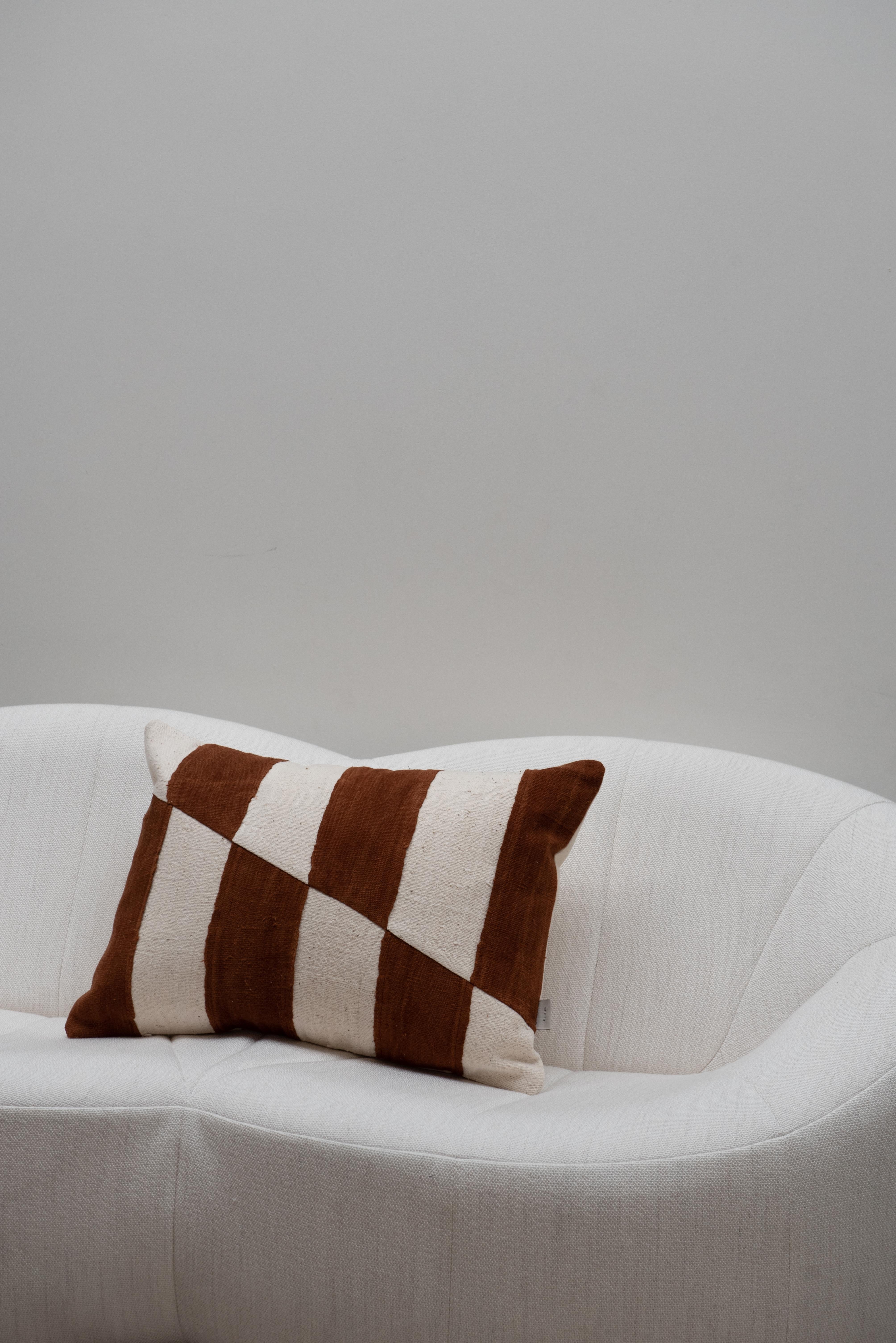 This white fabric is handwoven and plant- dyed in the Dogon region of Mali. The cotton is traditionally handpicked, spun and woven into small strips, which can still be seen in this cushion. All final designs and manufacturing takes place in a small