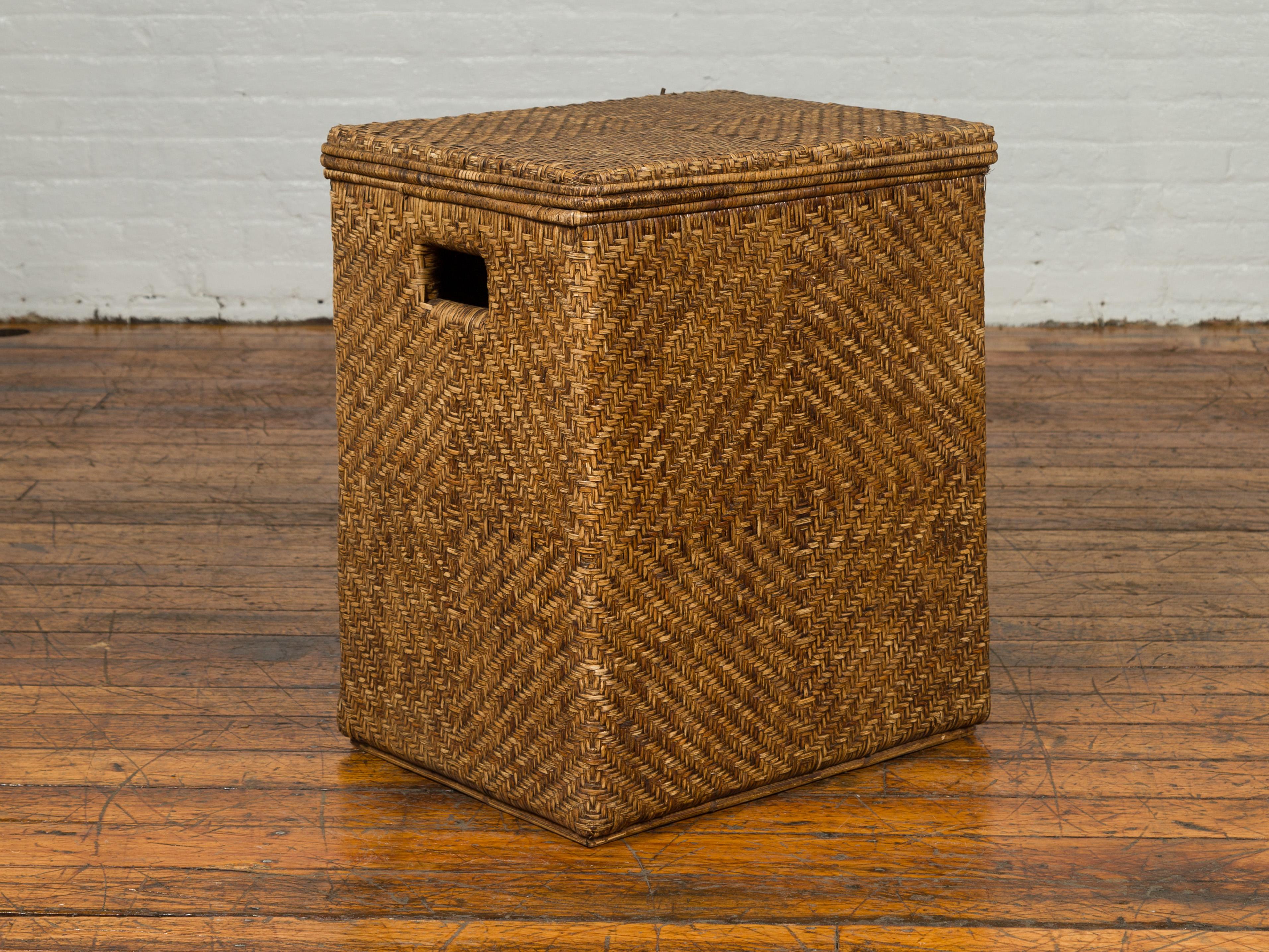 A Burmese handwoven rattan clothes hamper with pierced handles and lid. Crafted in Myanmar, this handwoven rattan hamper features a rectangular lid sitting above a linear body pierced on the sides to allow the piece to be moved more easily.
